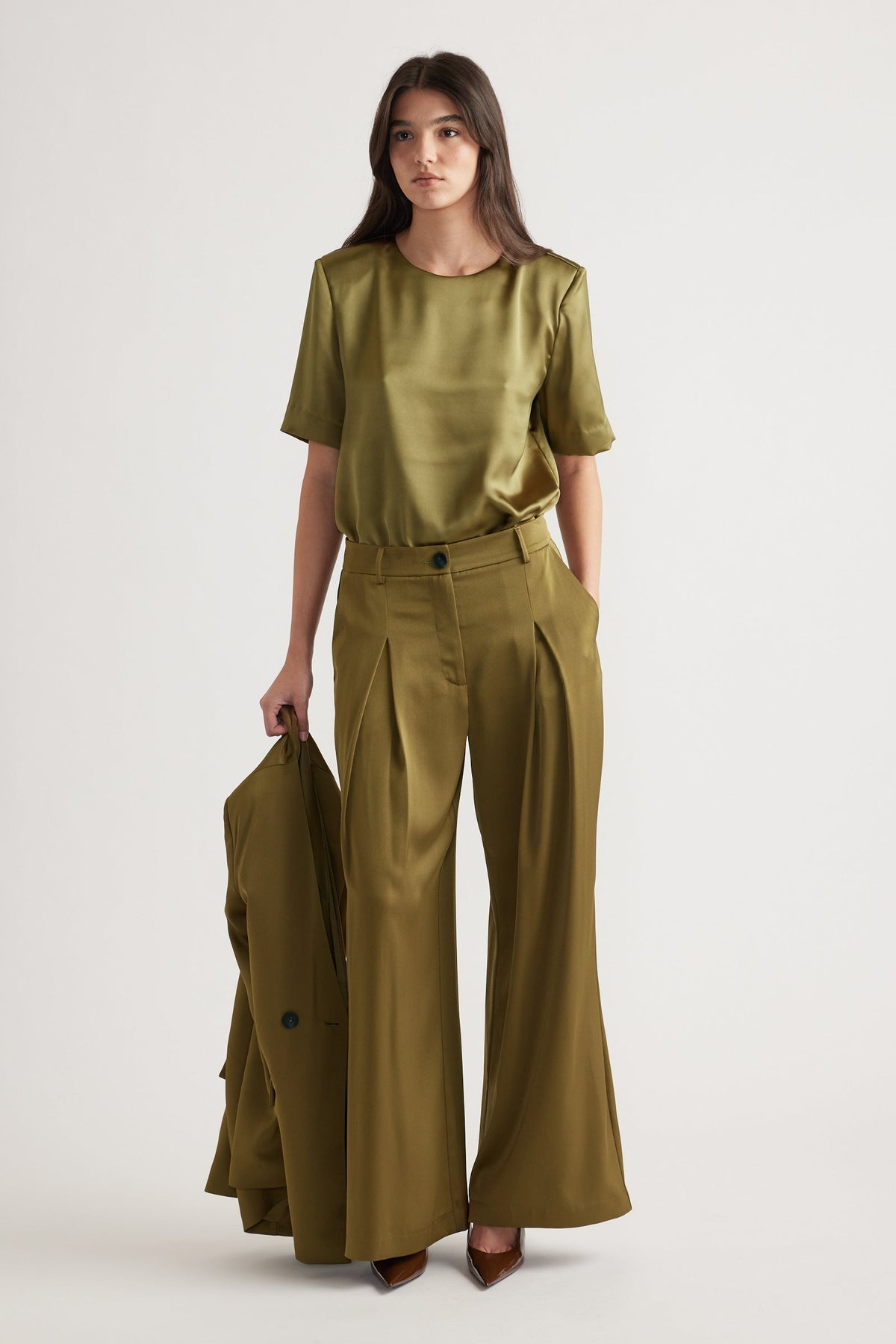 Woman wearing a chartreuse satin top with structured shoulders paired with high-waisted wide-leg trousers and pointed heels.
