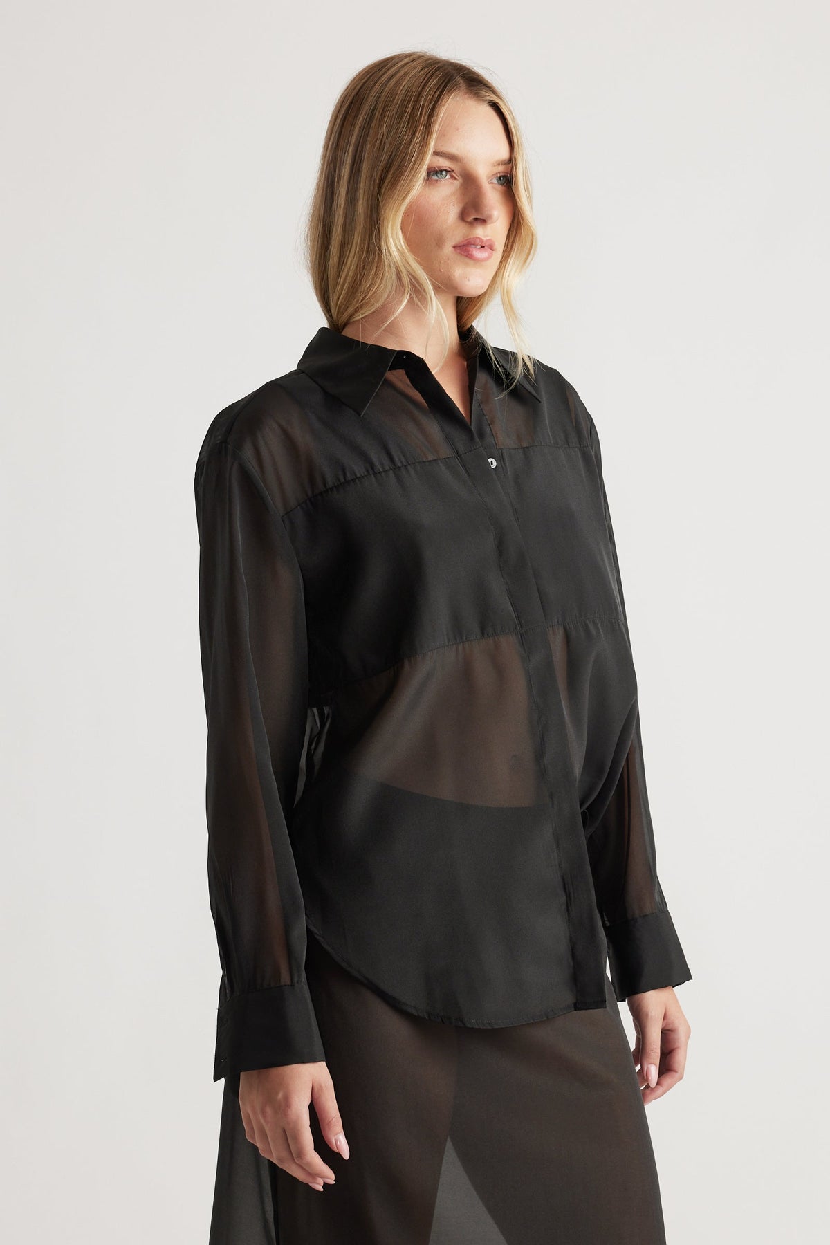 Woman wearing a black sheer organza shirt with long sleeves and a classic collar, styled in a relaxed fit