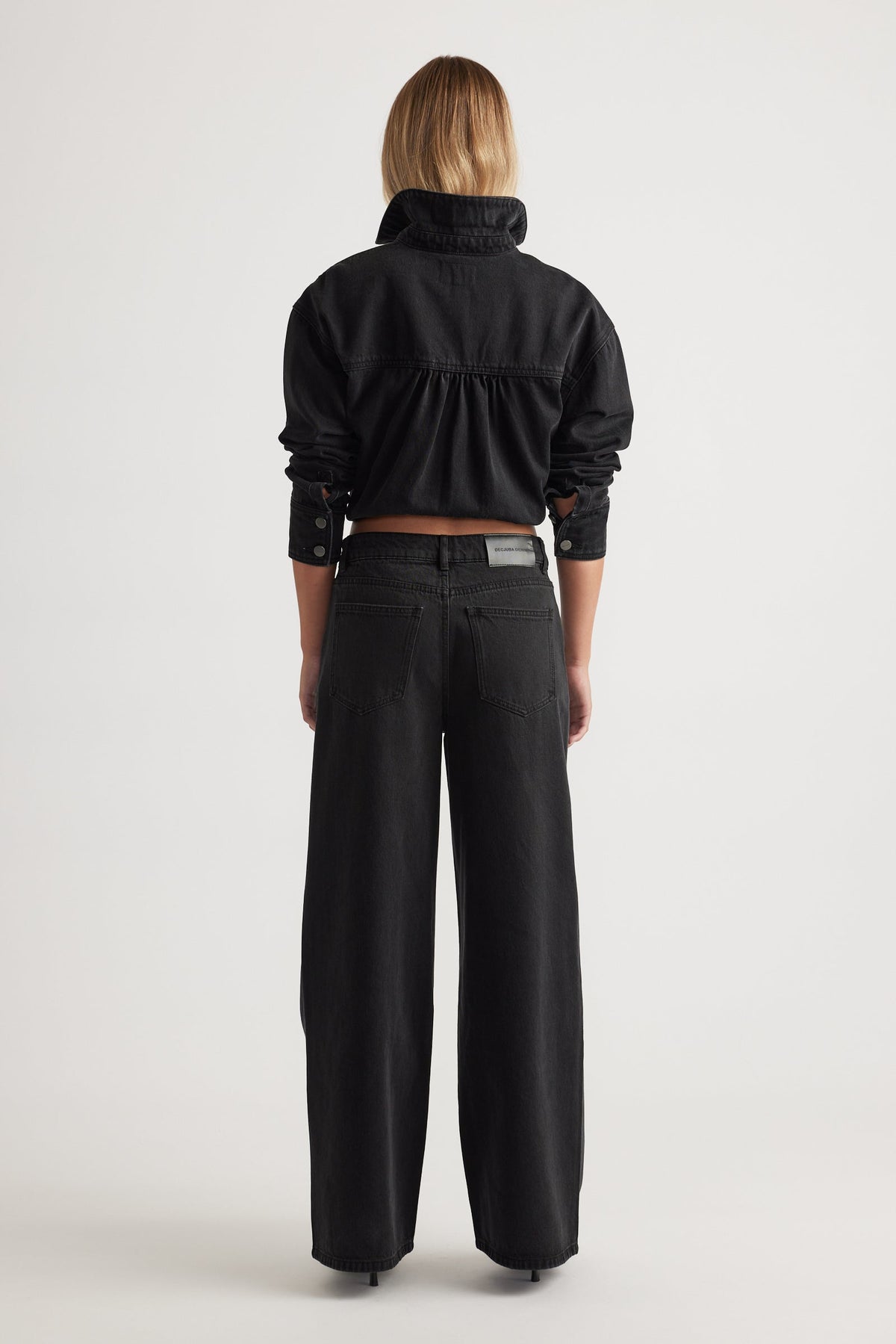 Back view of a woman wearing black Elena Wide Leg Jean styled with a cropped black shirt by DECJUBA.