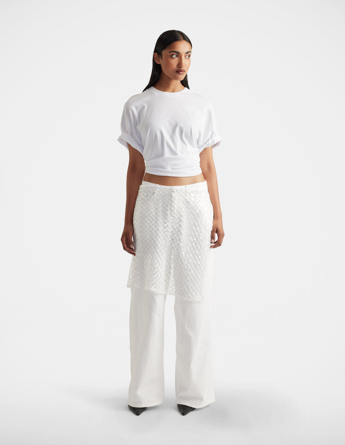 Woman wearing a white short-sleeve top paired with textured white layered pants and black pointed shoes