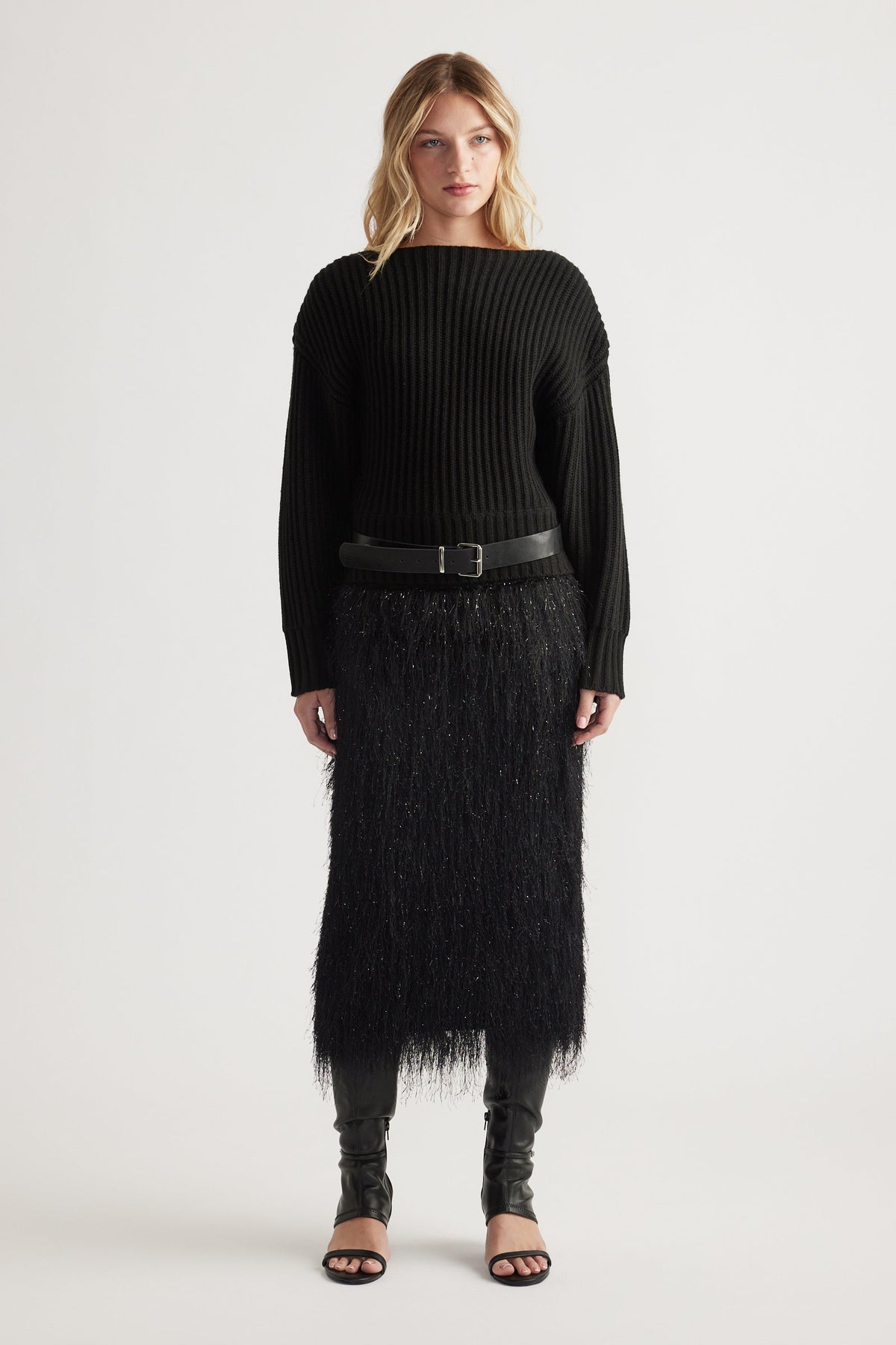 Woman wearing a black ribbed knit jumper with drop shoulders paired with a textured midi skirt and open-toe heels