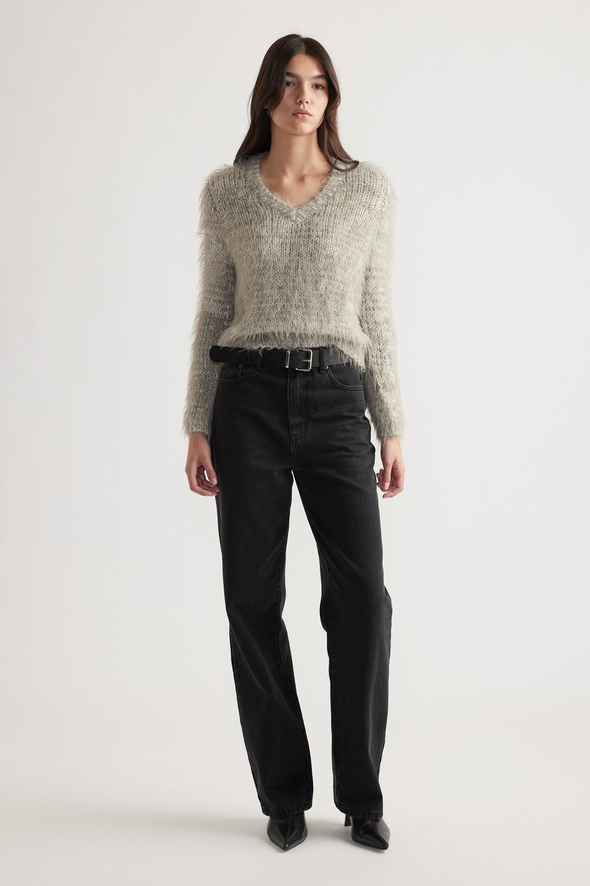 Woman standing wearing a soft textured V-neck knit jumper paired with high-waisted black jeans and pointed boots