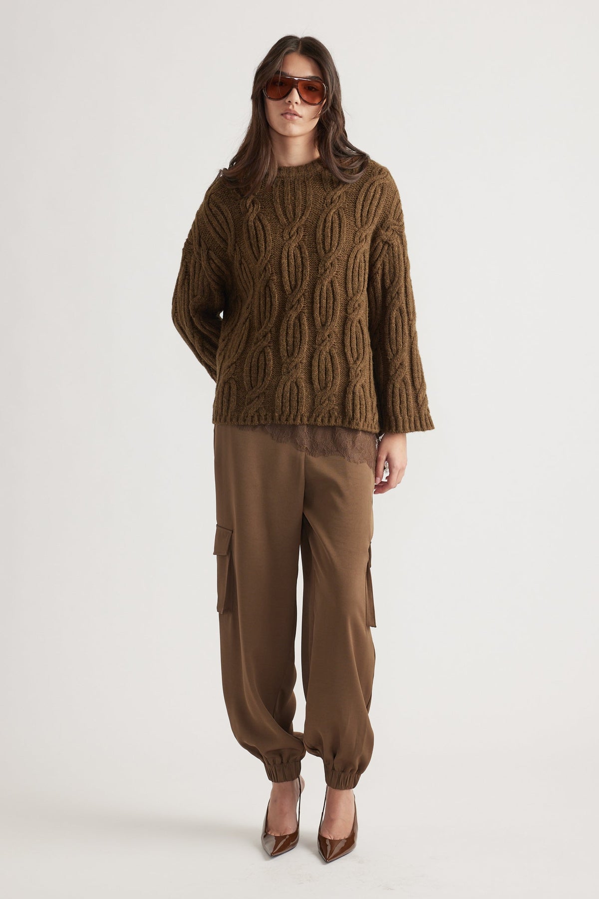 Woman wearing a textured cable knit jumper in bronze paired with relaxed cargo pants and brown pointed heels, styled with oversized sunglasses