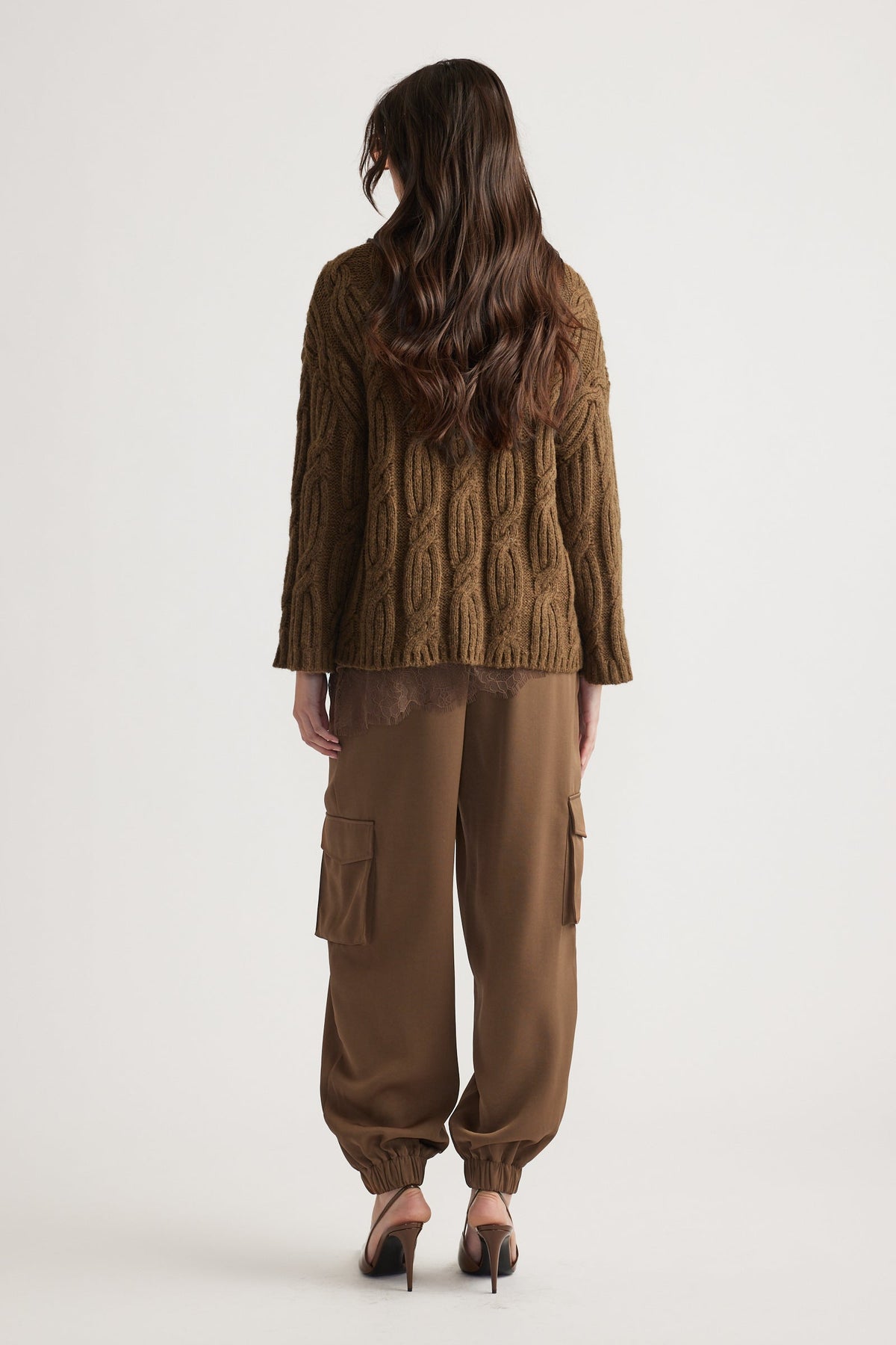 Woman seen from behind wearing a textured brown cable knit jumper paired with relaxed cargo pants and heels