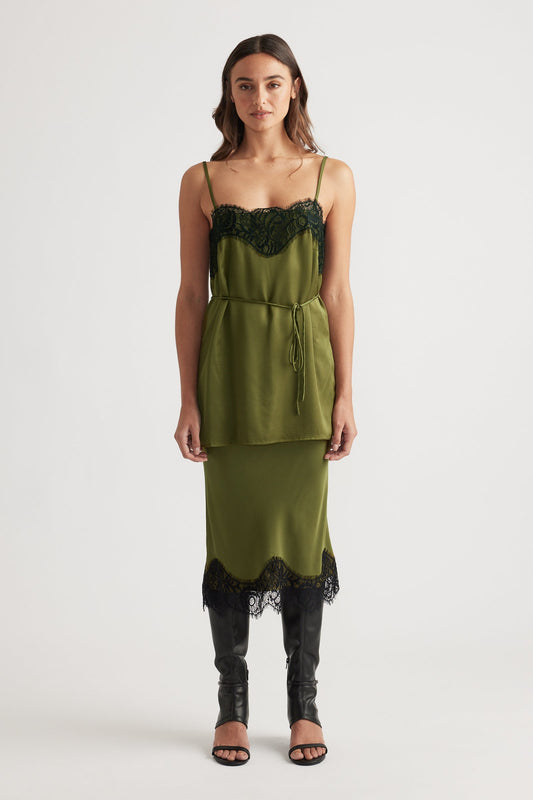 Front view of an olive green lace-trimmed slip dress layered with a matching tied waist top and black heeled boots