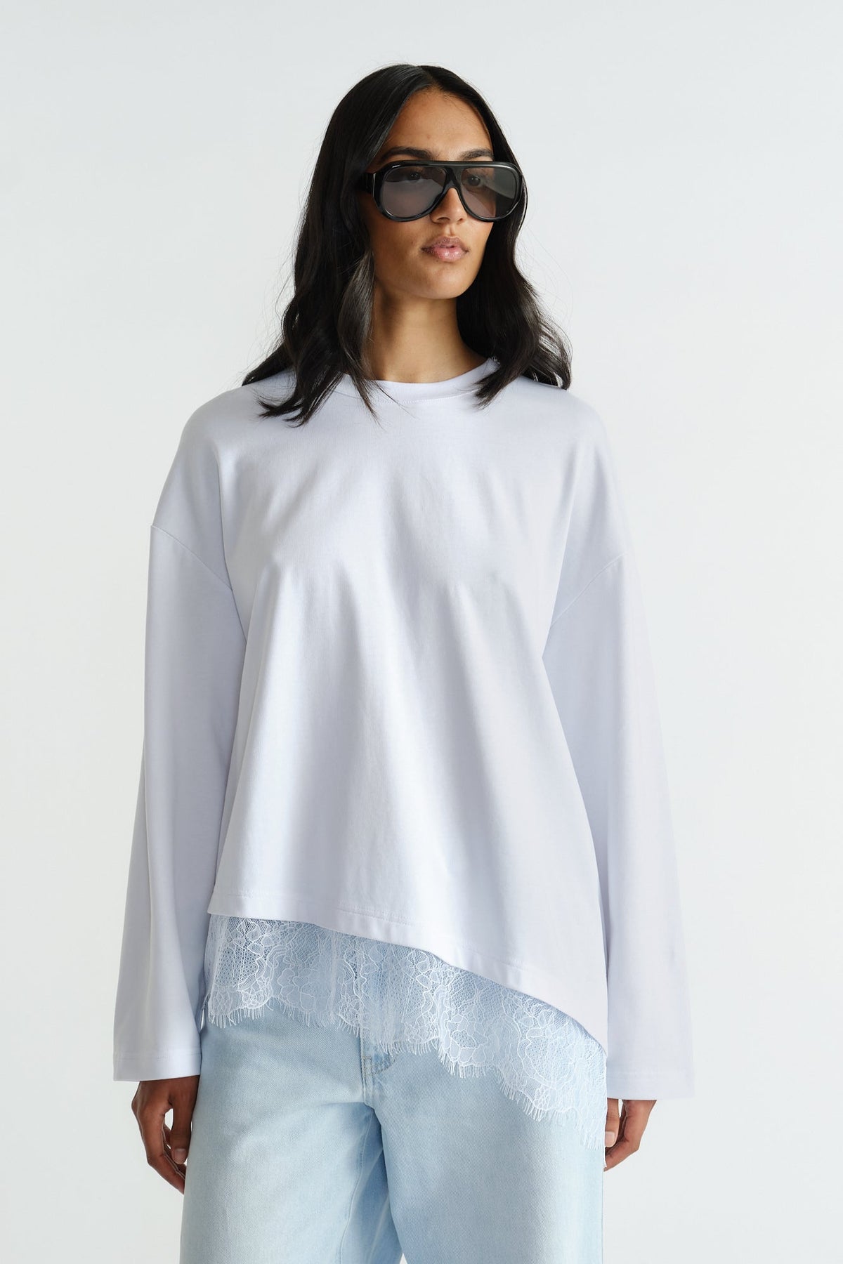 Woman wearing relaxed white long sleeve top with delicate lace trim and light wash denim jeans and oversized sunglasses