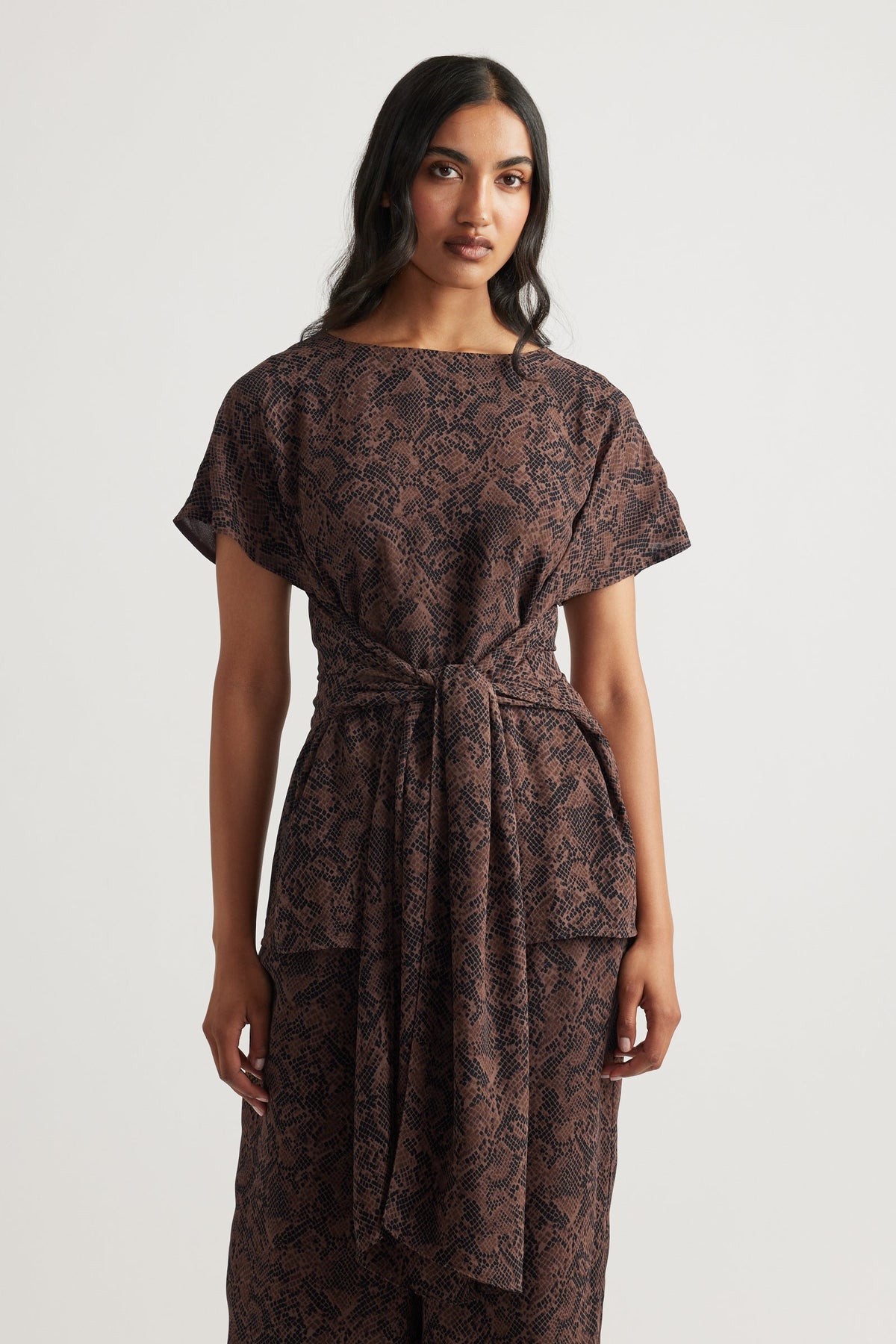 Woman wearing a brown snake-print tie tunic with short sleeves and a relaxed fit, styled for effortless elegance
