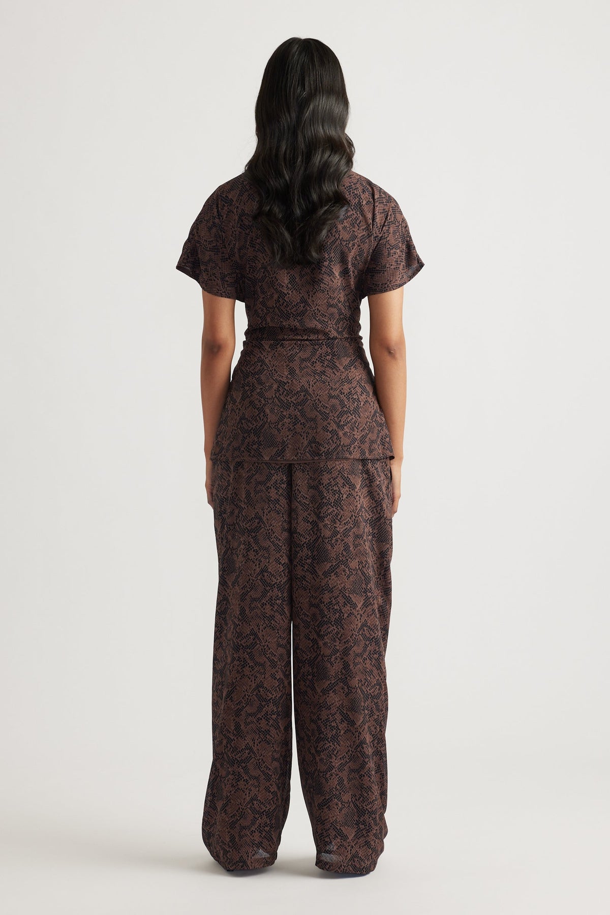 Woman wearing a dark brown tie tunic and matching wide-leg pants with a subtle snake pattern in a relaxed silhouette