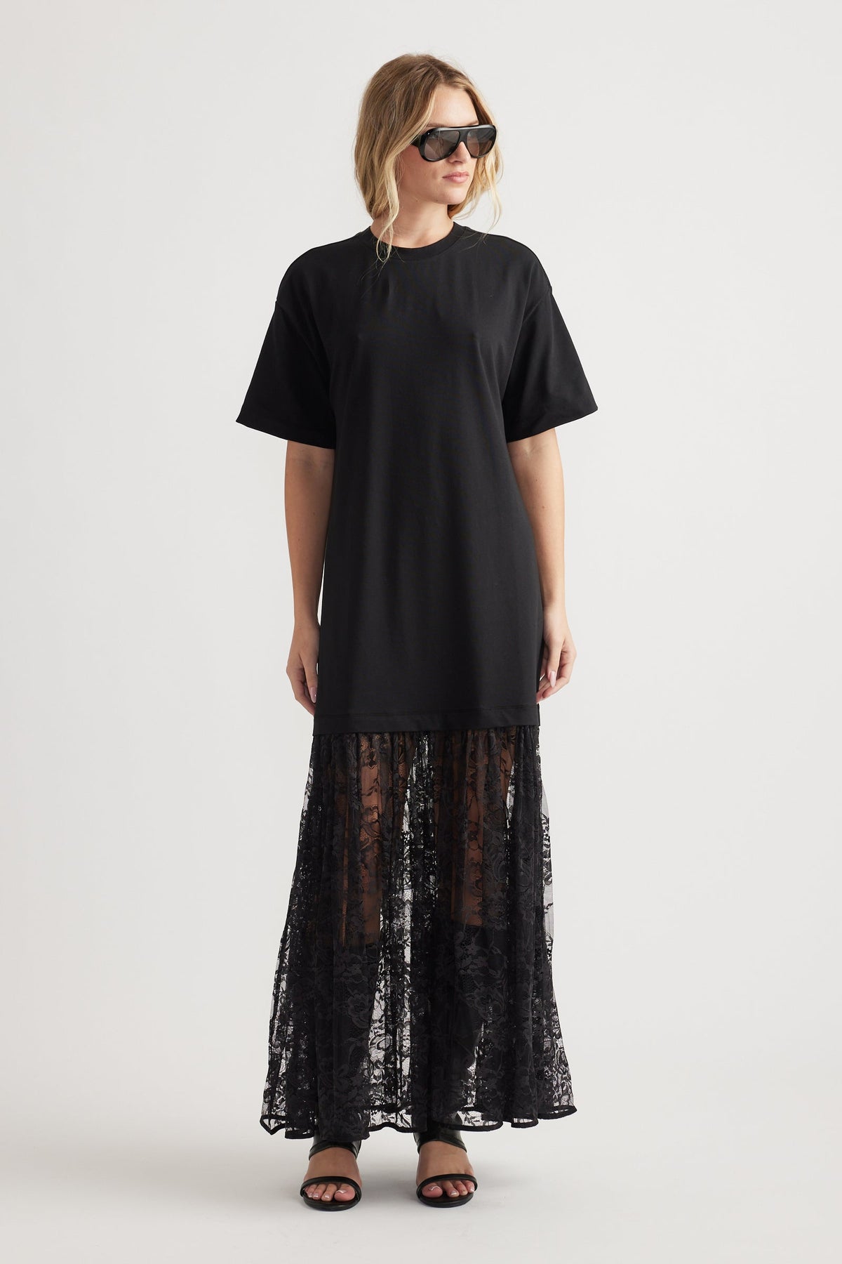 Woman wearing a black crew neck dress with short sleeves and a sheer lace maxi skirt paired with black sandals