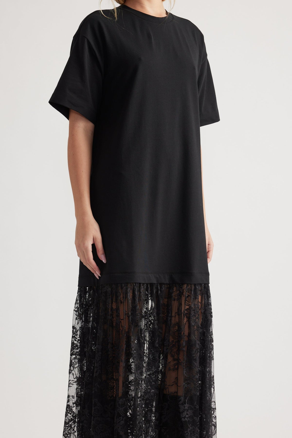 Woman wearing black short sleeve dress with crew neck and sheer lace maxi skirt panel at hem