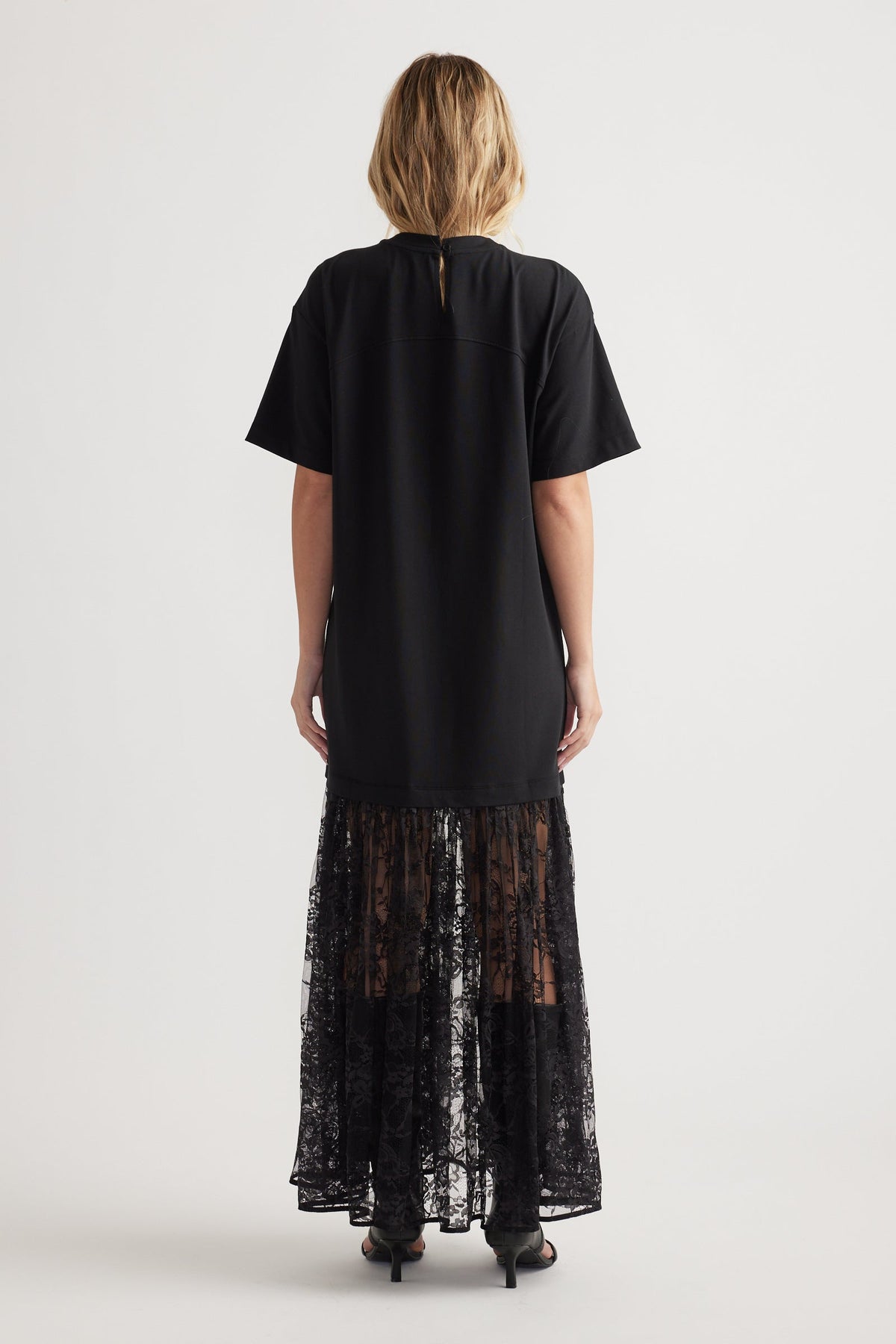 Rear view of woman wearing black short sleeve dress with a solid top and sheer spliced lace maxi skirt panel