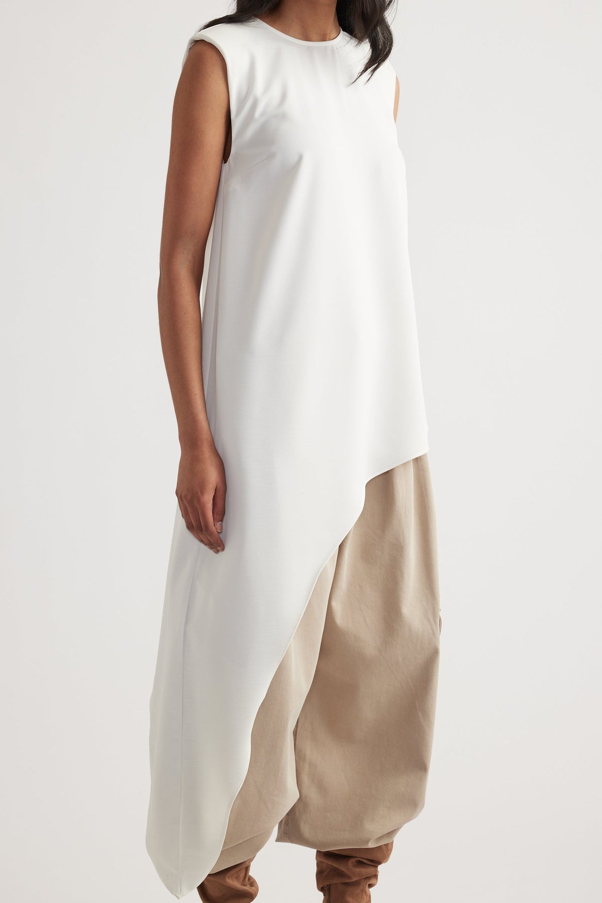Woman wearing a sleeveless ivory drape top with an asymmetrical hem over loose beige pants for a relaxed look