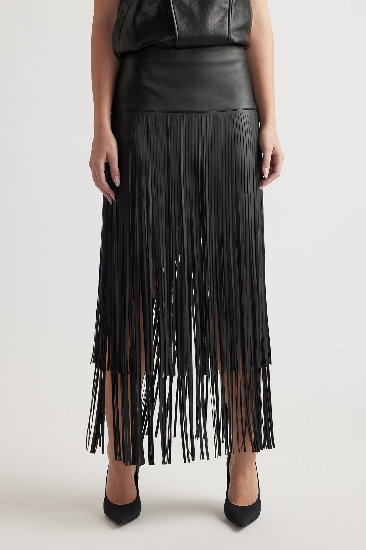 Front view of a fitted high-waist black skirt with tiered fringe detailing paired with black pointed heels