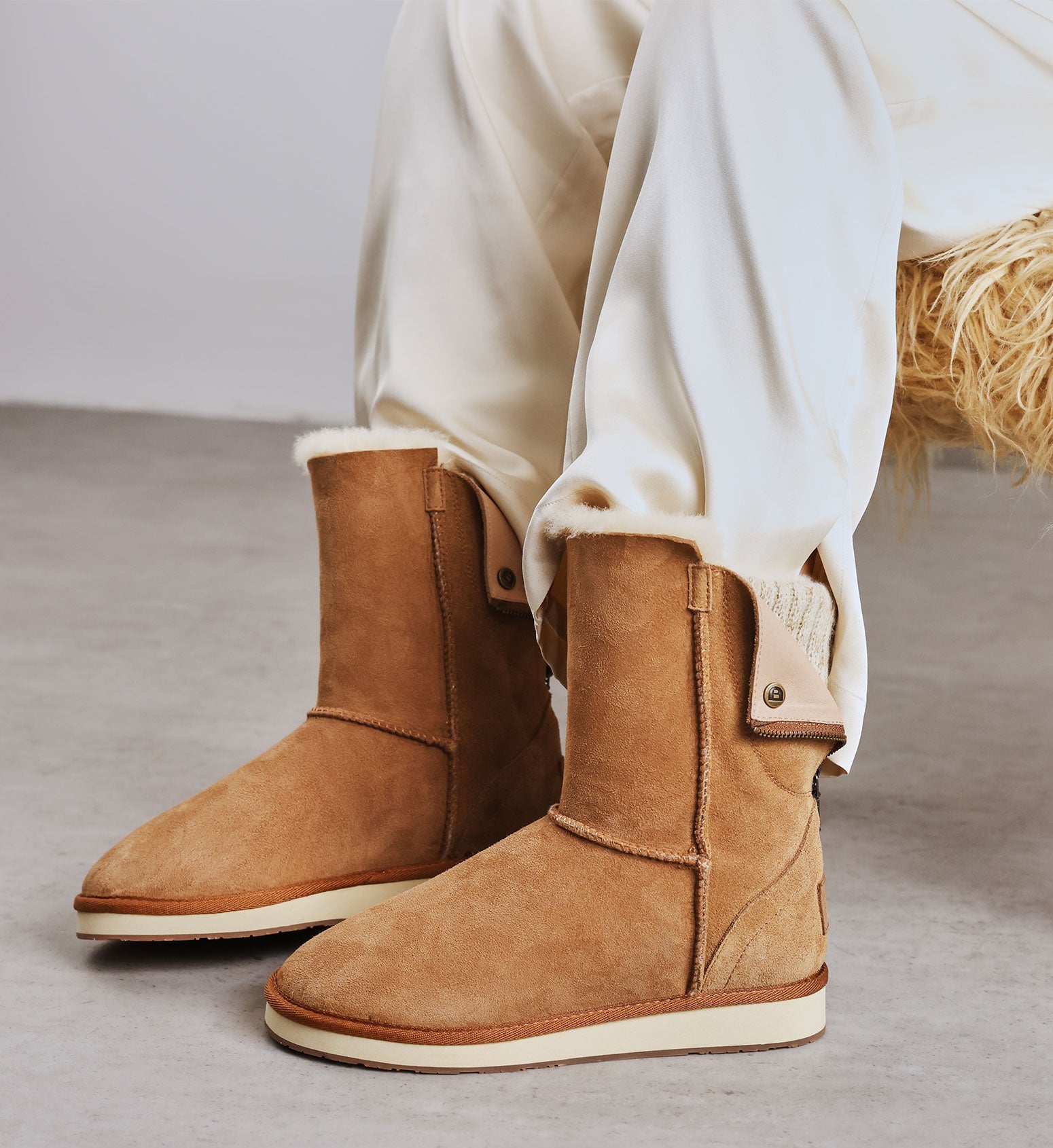 Tan suede boots with white soles worn with white pants on a neutral background.