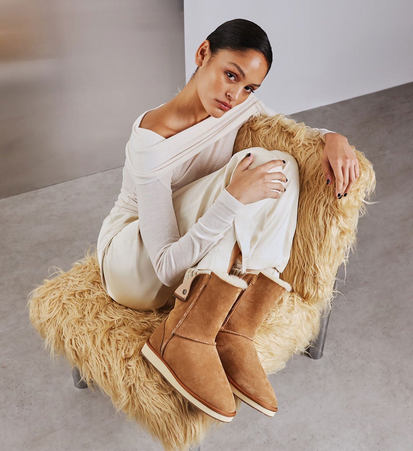 woman sitting on a furry chair wearing brown slipper boots with a cream outfit