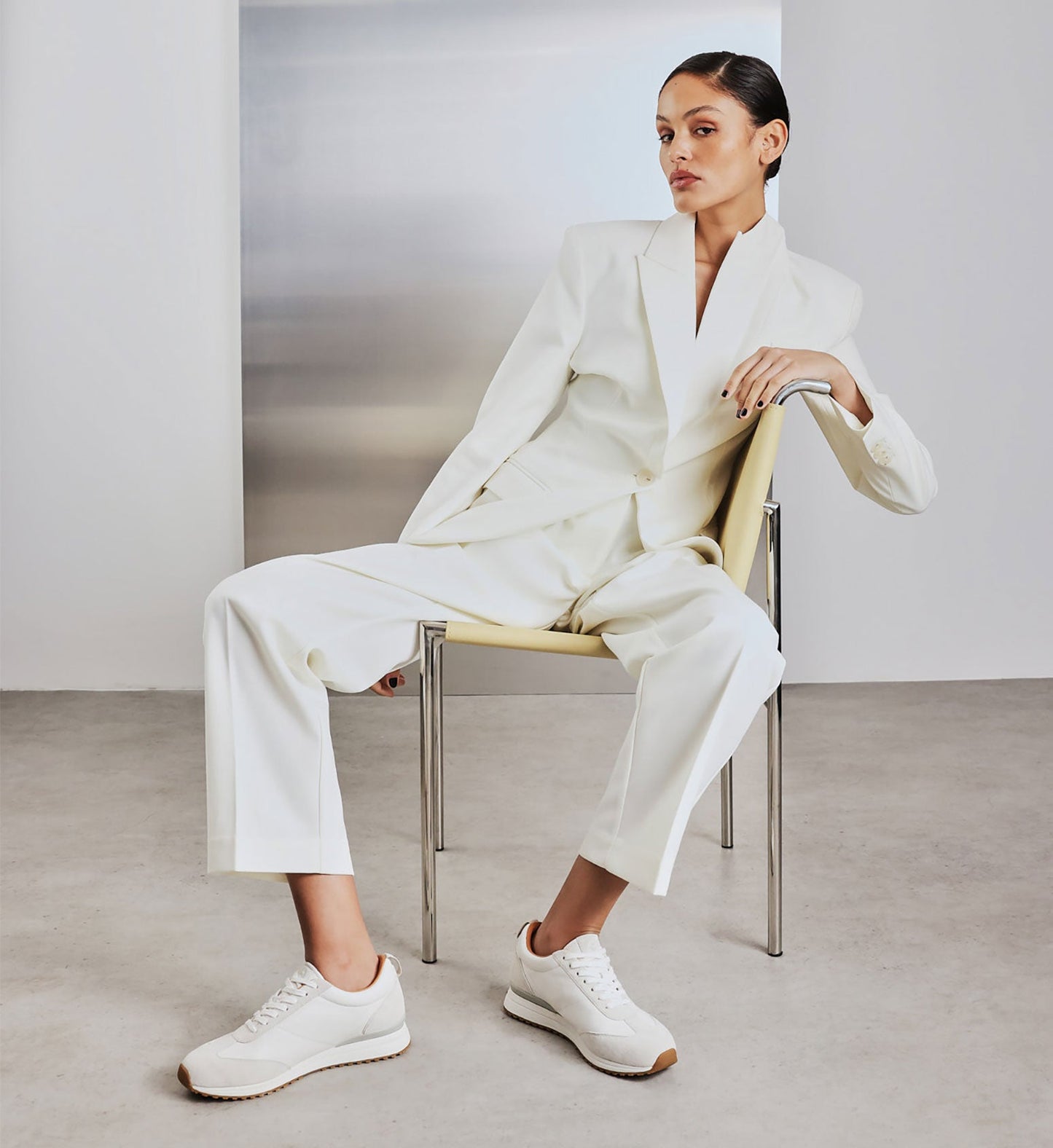 woman sitting in a chair wearing a white suit and white sneakers