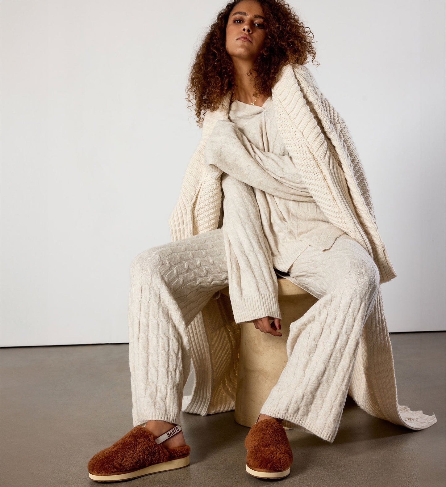 model wearing a cream knit matching outfit with a knitted robe and terracotta snuggling sheepskin slippers