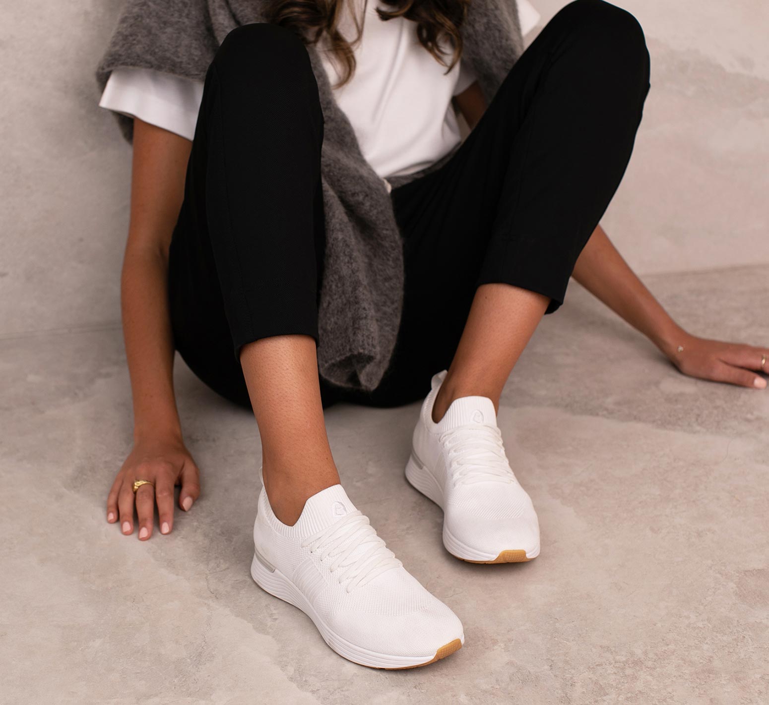 woman sitting on the ground wearing white knit sneakers, black pants and a white tshirt