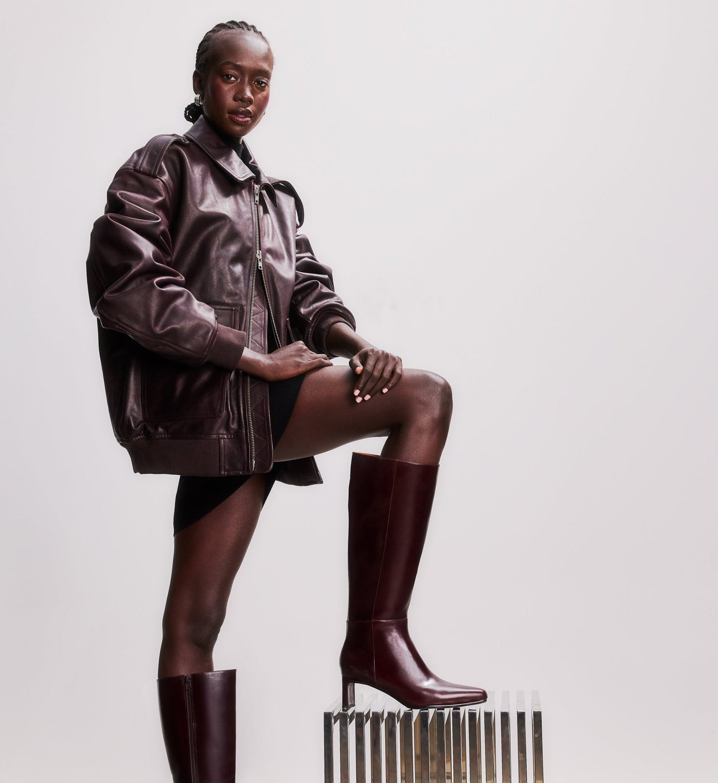 model standing on a stool wearing a brown leather jacket and brown knee high boots
