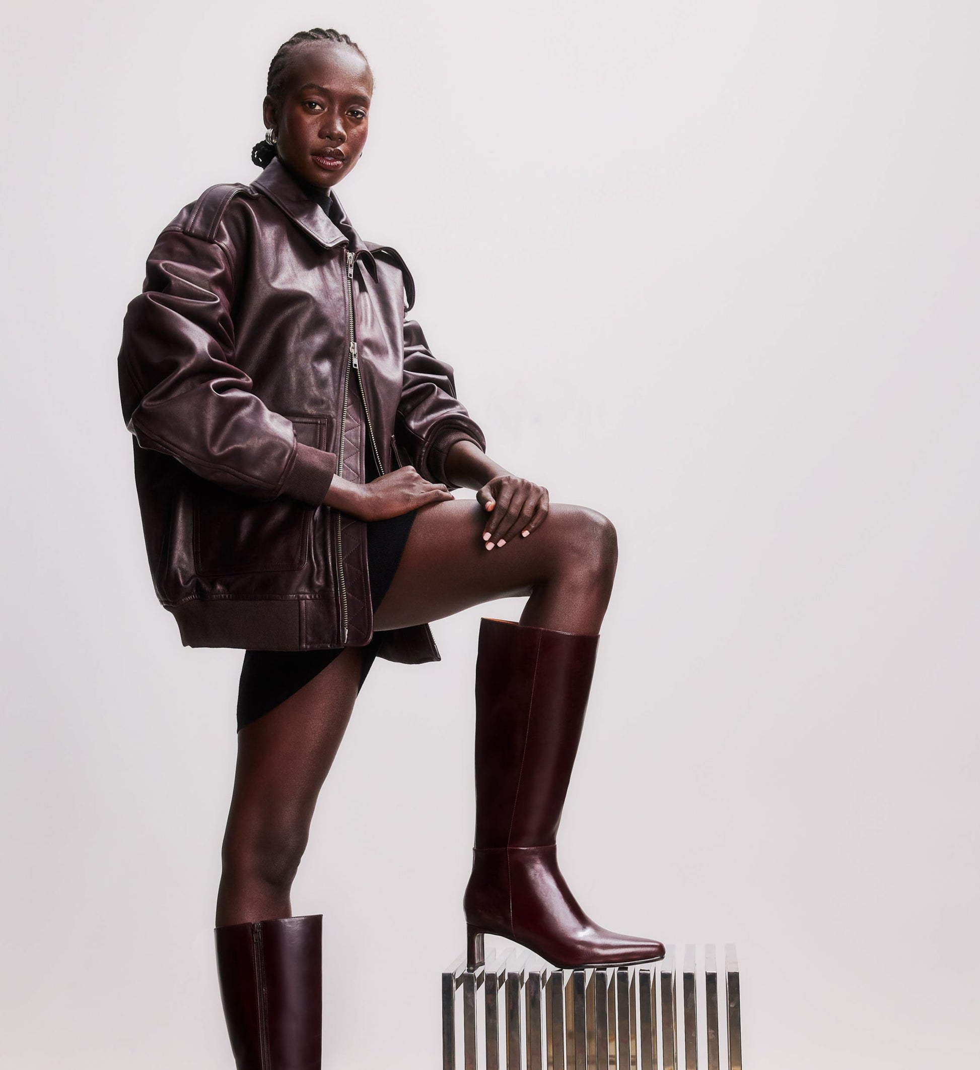 model standing on a stool wearing a brown leather jacket and brown knee high boots