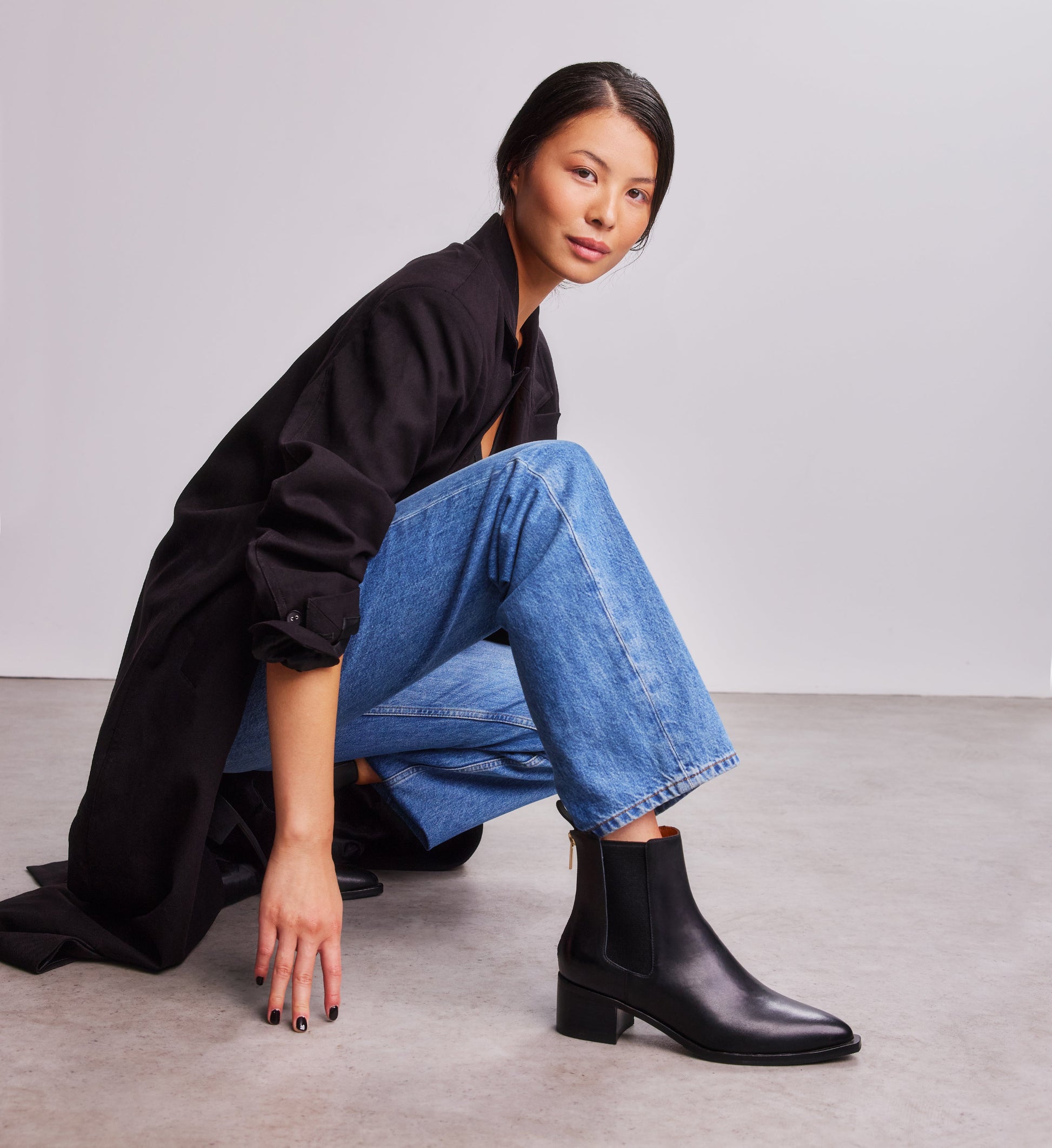 woman wearing black chelsea boots, denim jeans and a black coat