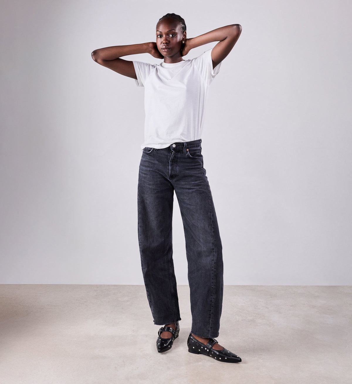 Person wearing a white t-shirt and dark jeans with black studded mary janes against a plain background