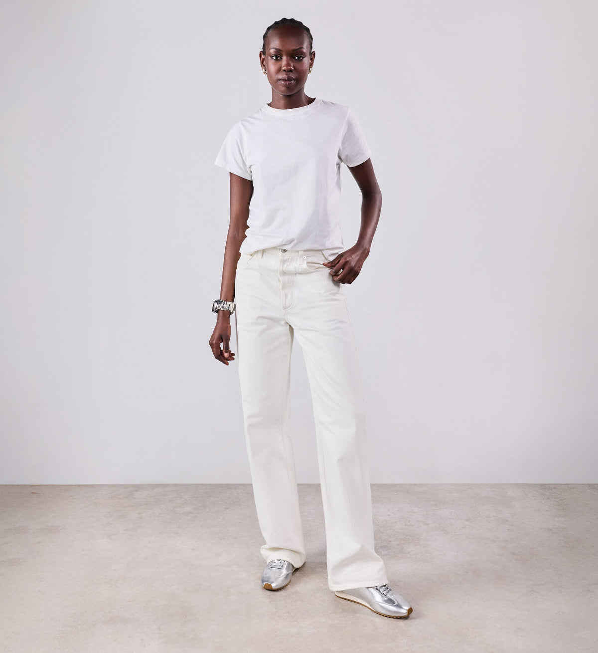 Person wearing a white t-shirt and white pants standing against a plain background with silver sneakers