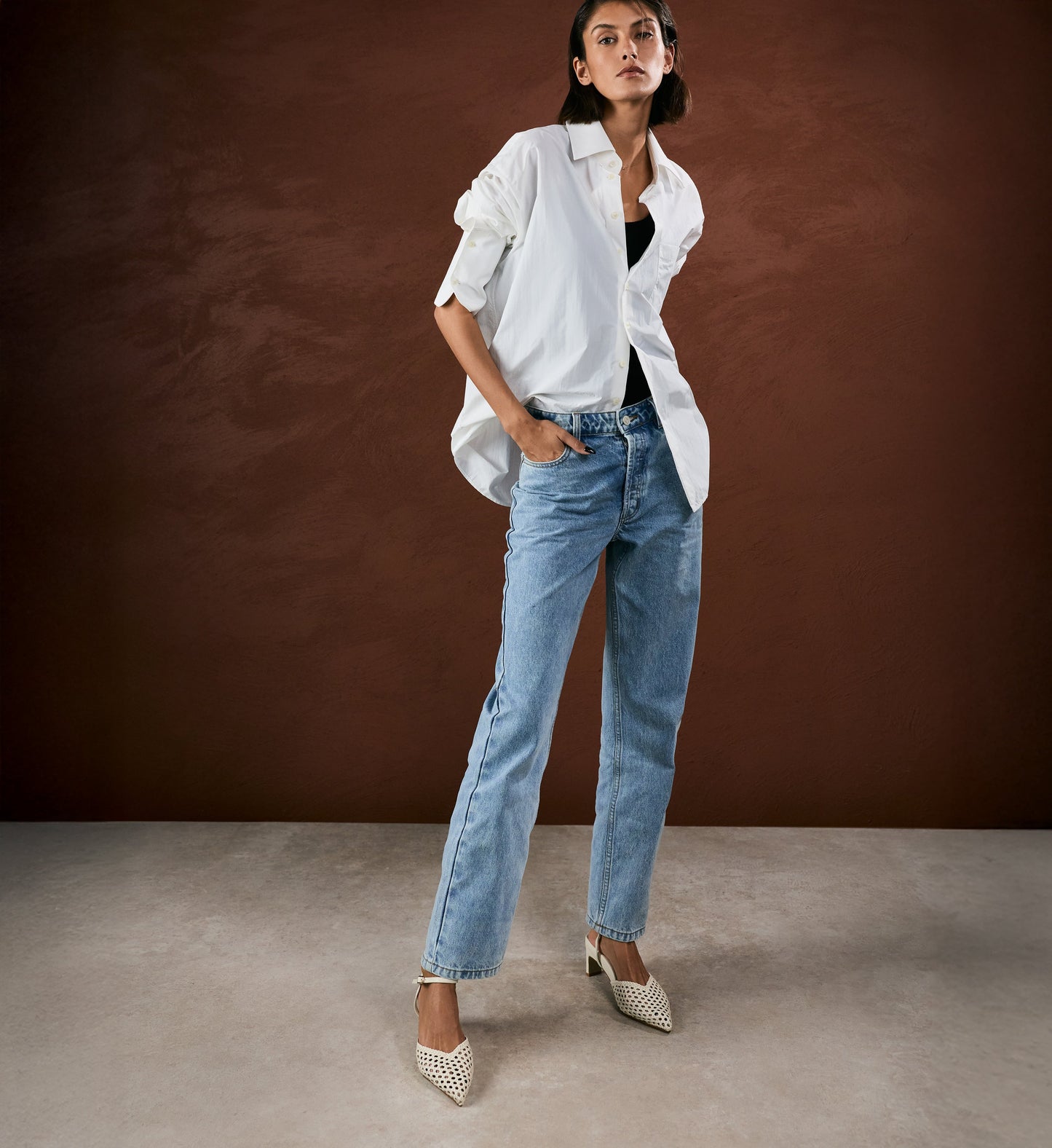 Woman wearing a white shirt and blue jeans against a brown background