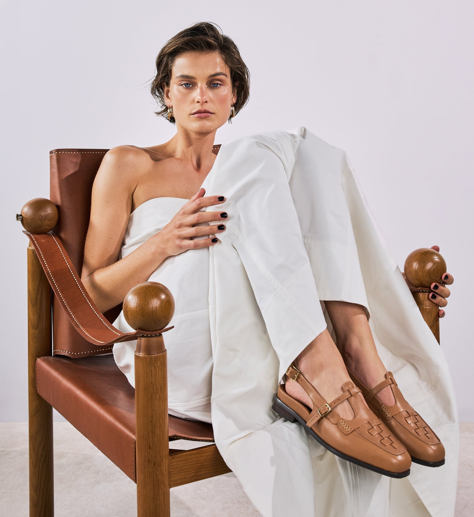 Woman sitting on a brown chair wearing white pants and brown woven leather loafers