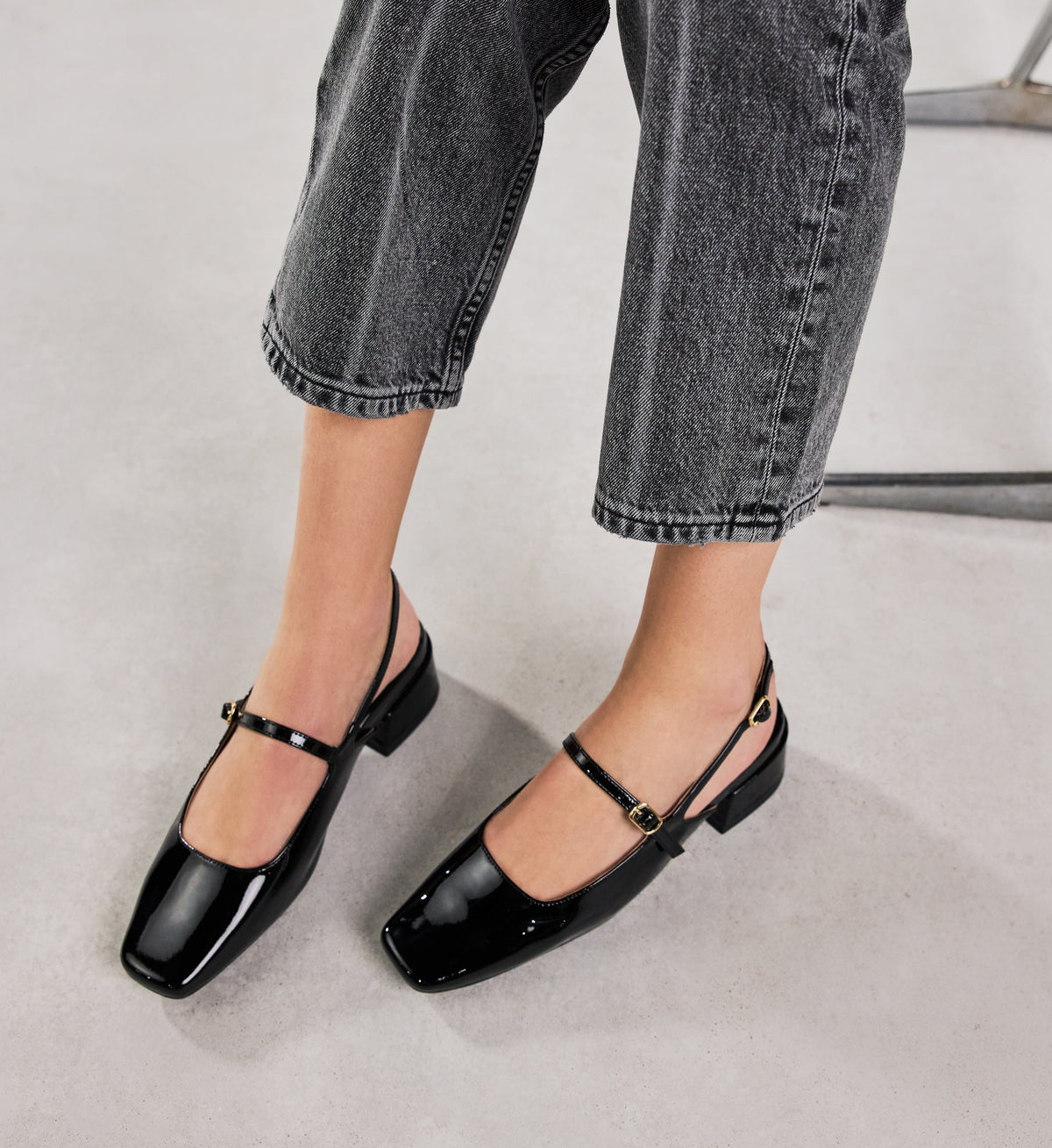 Black patent leather shoes worn with black jeans on a light gray background