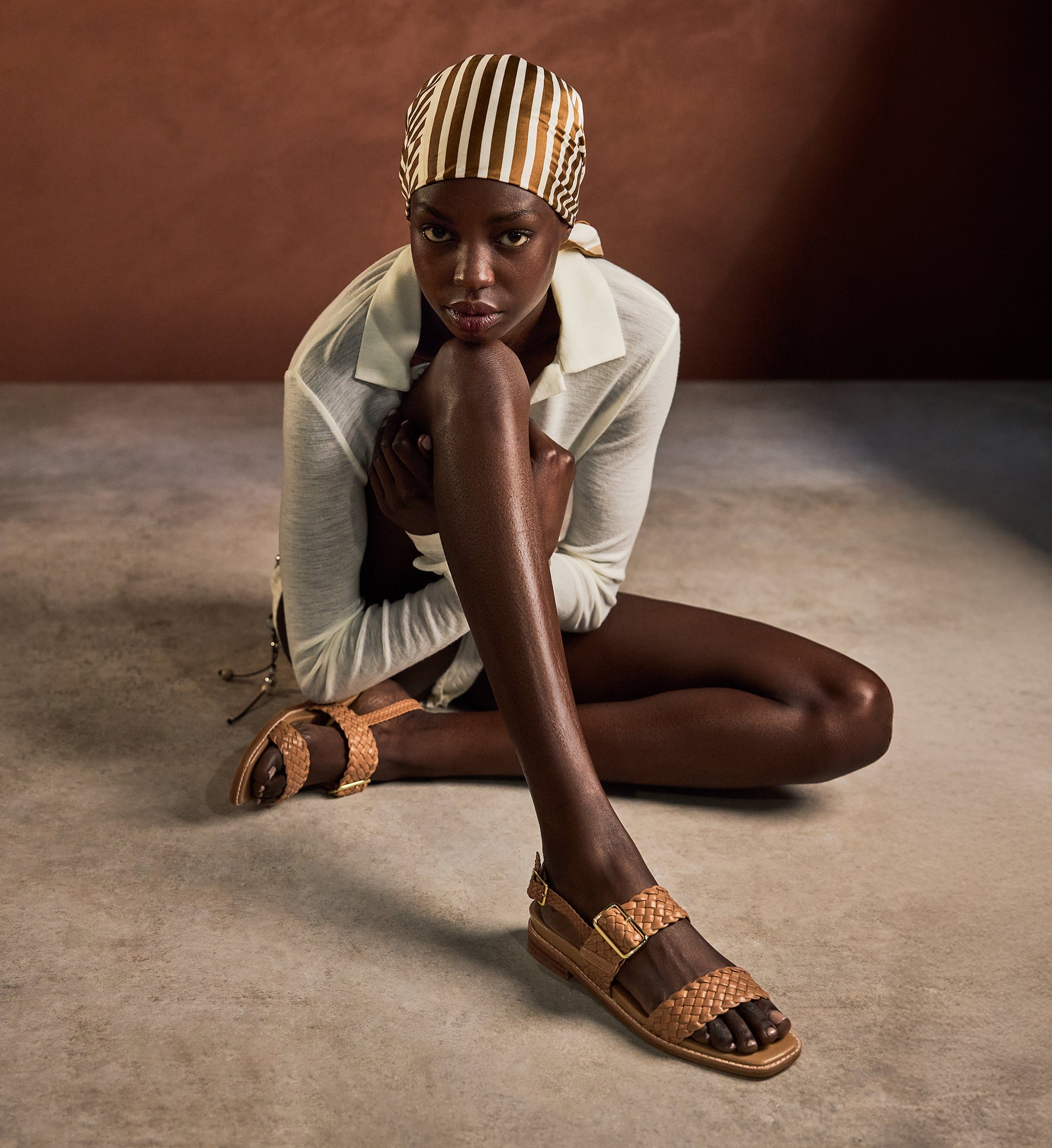 Woman wearing a striped headscarf and tan sandals sitting on a textured floor.