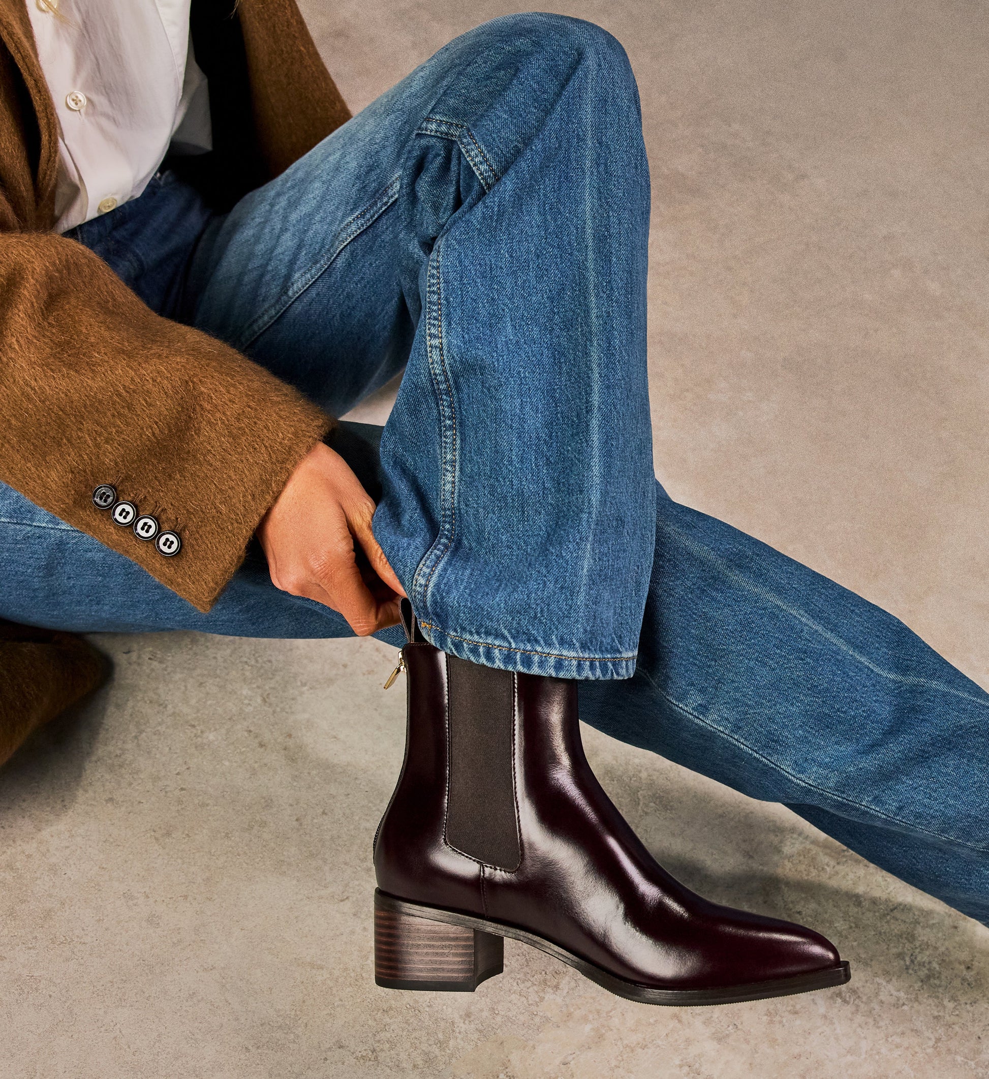 Person wearing brown leather ankle boots and blue jeans on a neutral background