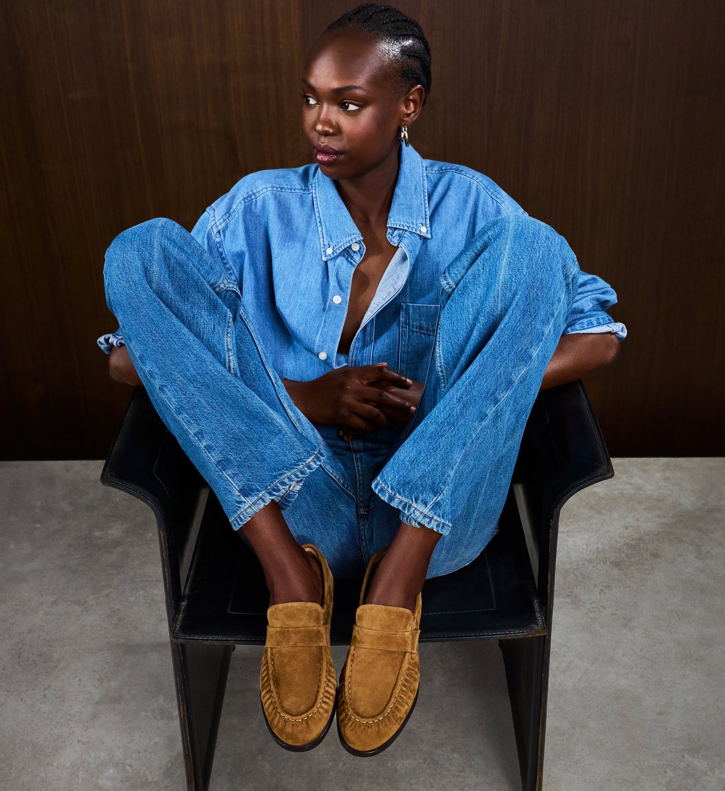 Person wearing a blue denim outfit with brown shoes sitting on a chair.