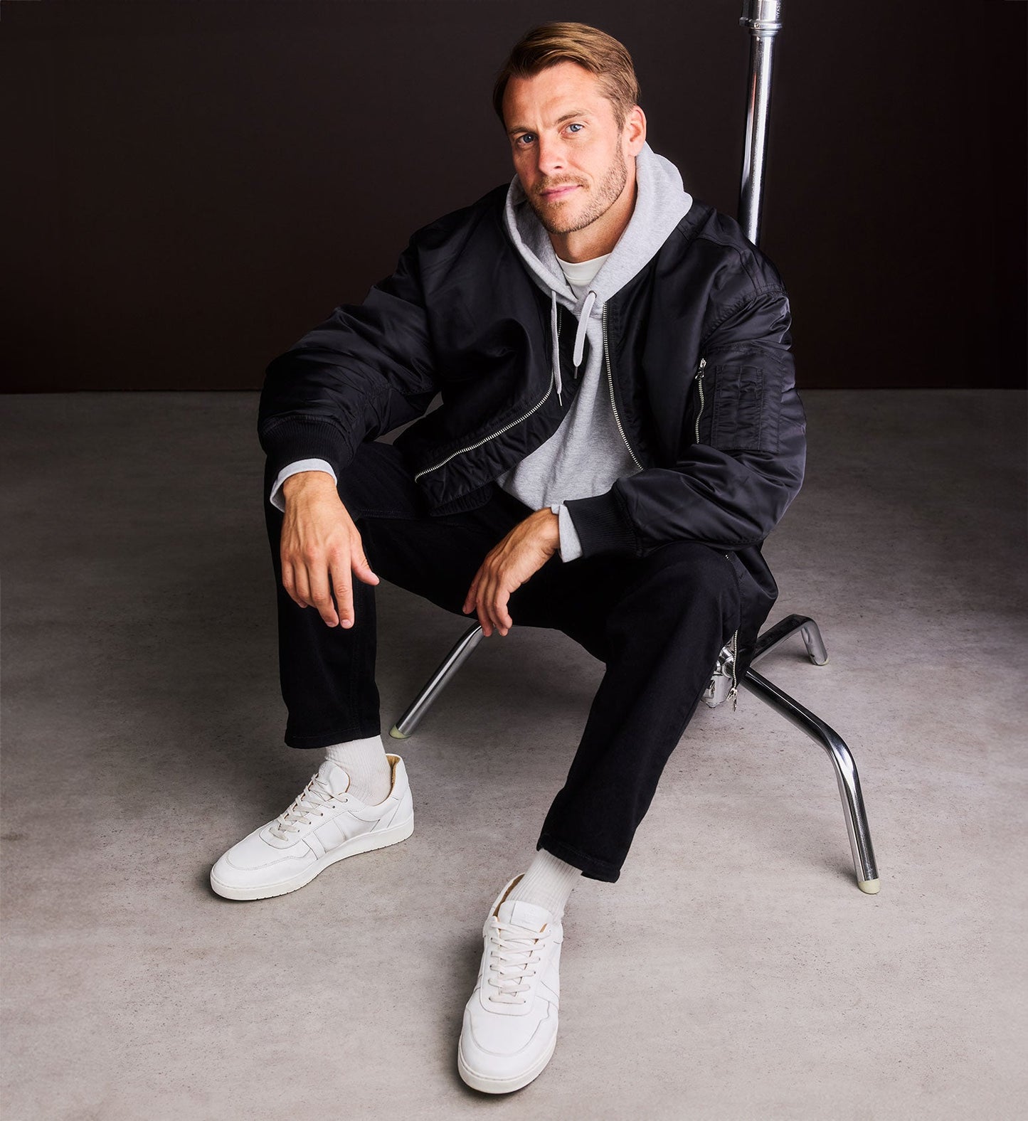 man wearing white sneakers with a black bomber jacket, grey hoodies and black pants