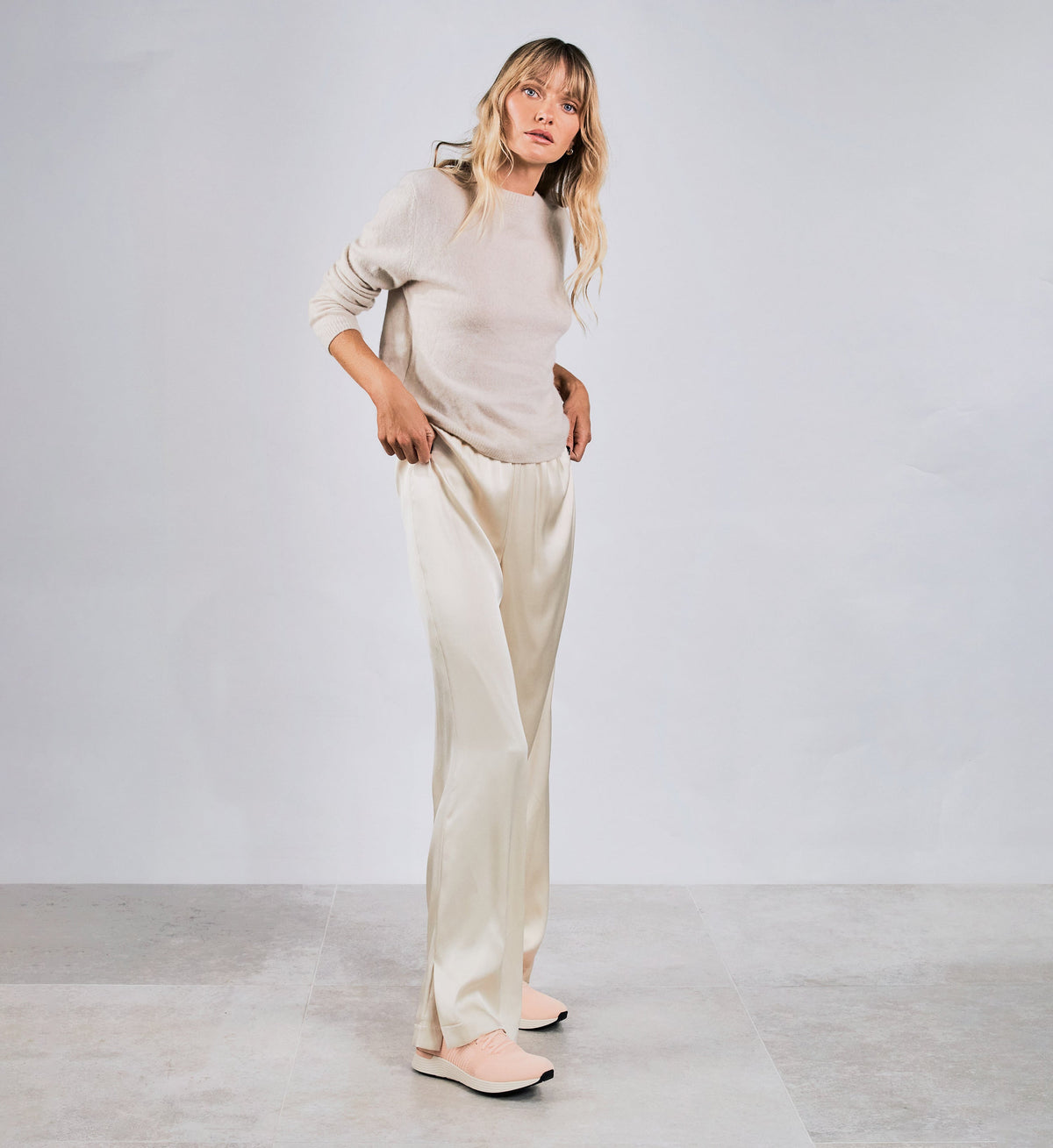 Woman wearing a beige outfit standing against a plain white background with pink sneakers