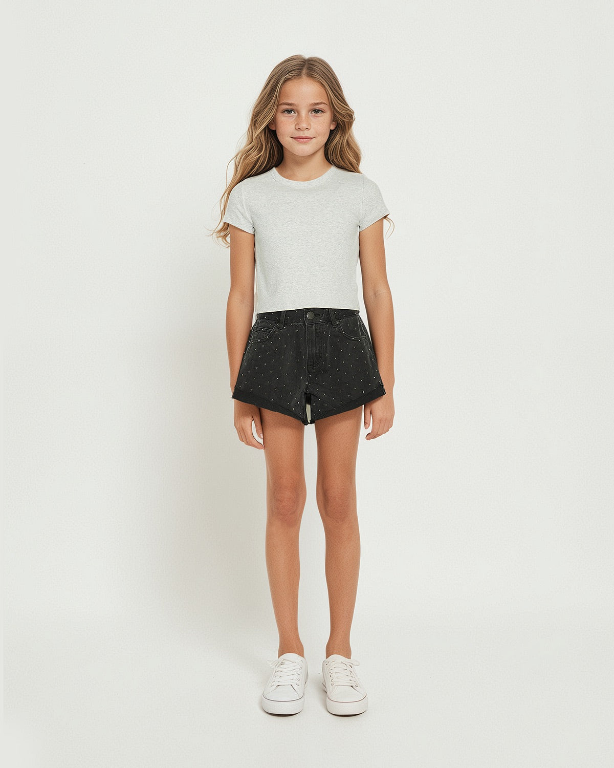 Young girl wearing black rhinestone-embellished shorts paired with a simple light grey tee and white sneakers.