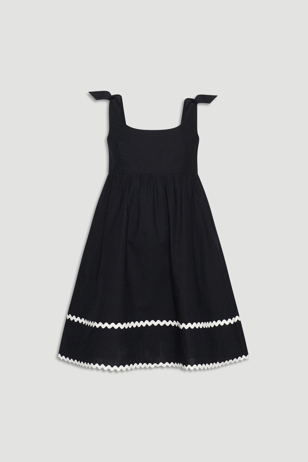 Black sleeveless girls mini dress with square neckline, tie shoulder straps, and white wavy trim near hem.