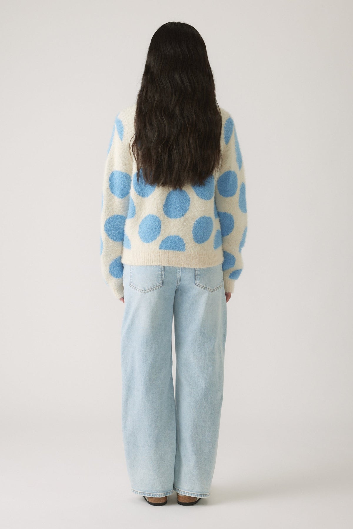 Rear view of girl wearing a cozy cream jumper with large blue polka dots paired with light blue wide-leg jeans