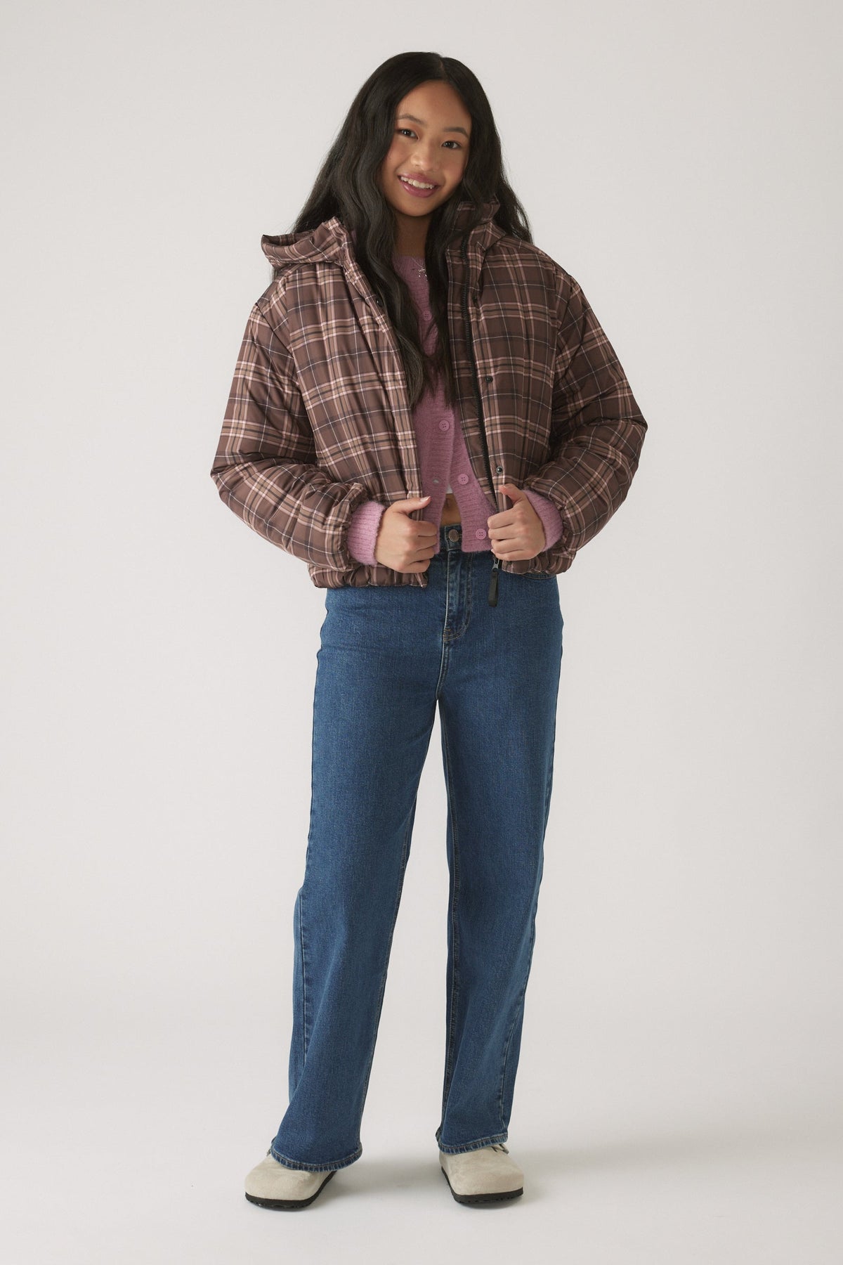 Girl wearing a brown check hooded puffer jacket over a lavender knit top and straight-leg blue jeans with casual shoes