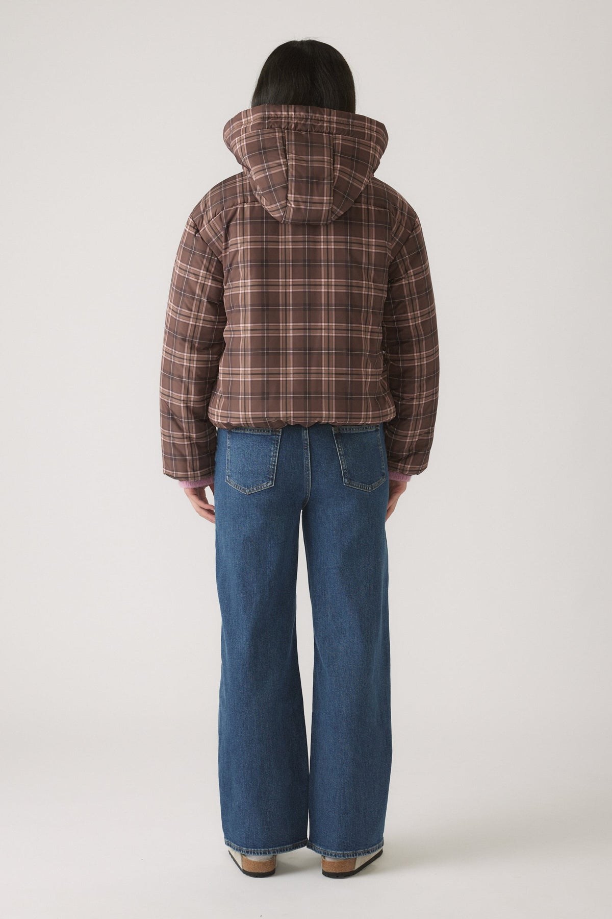Child seen from behind wearing a brown checked hooded puffer jacket paired with classic straight-leg blue jeans