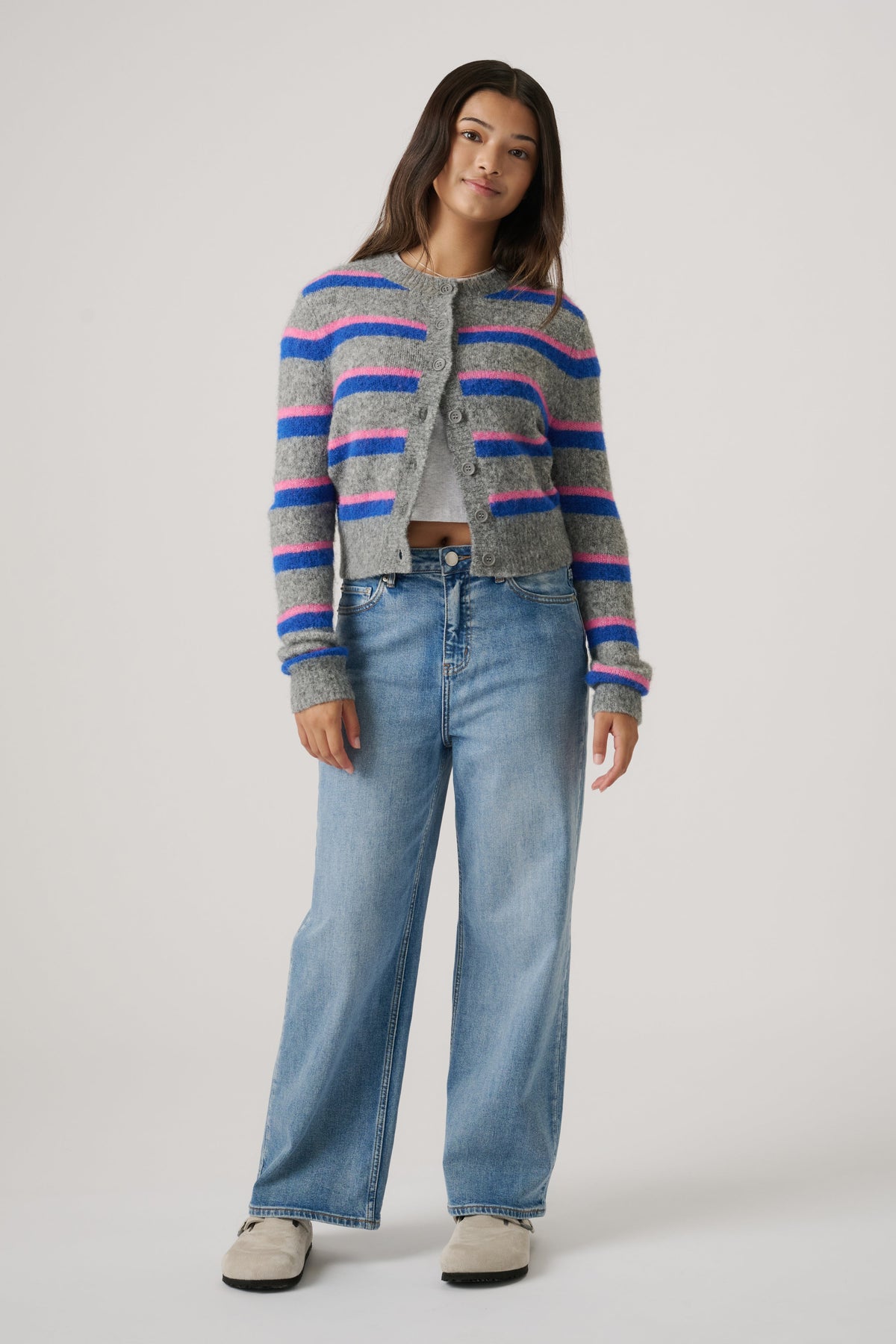 Teen girl wearing a cozy cropped cardigan with pink and blue stripes paired with loose light-wash denim jeans and beige shoes