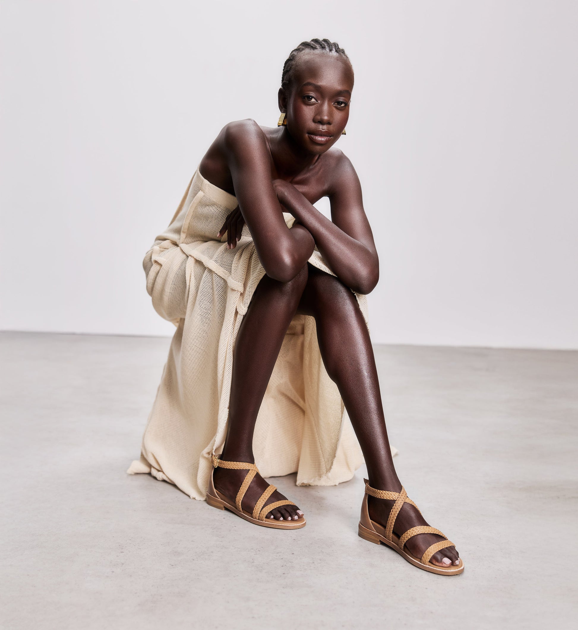 Model wearing tan strappy sandals and a beige dress on a white background