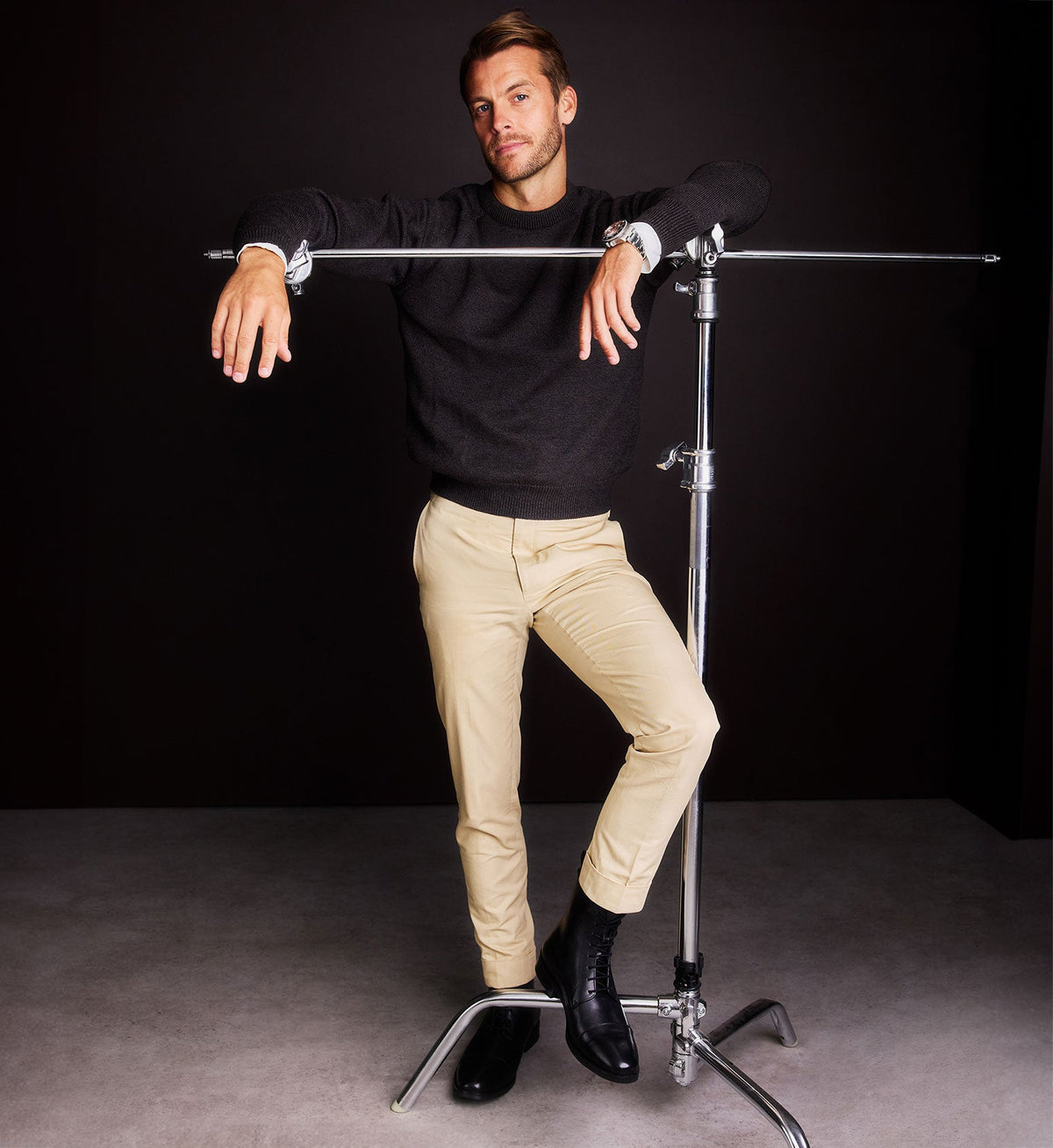 Man posing wearing black boots, beige pants and black jumper against a black background