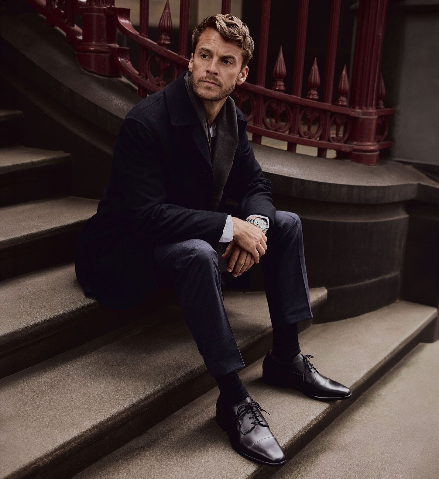 man sitting on stairs outside wearing black dress shoes and a suit