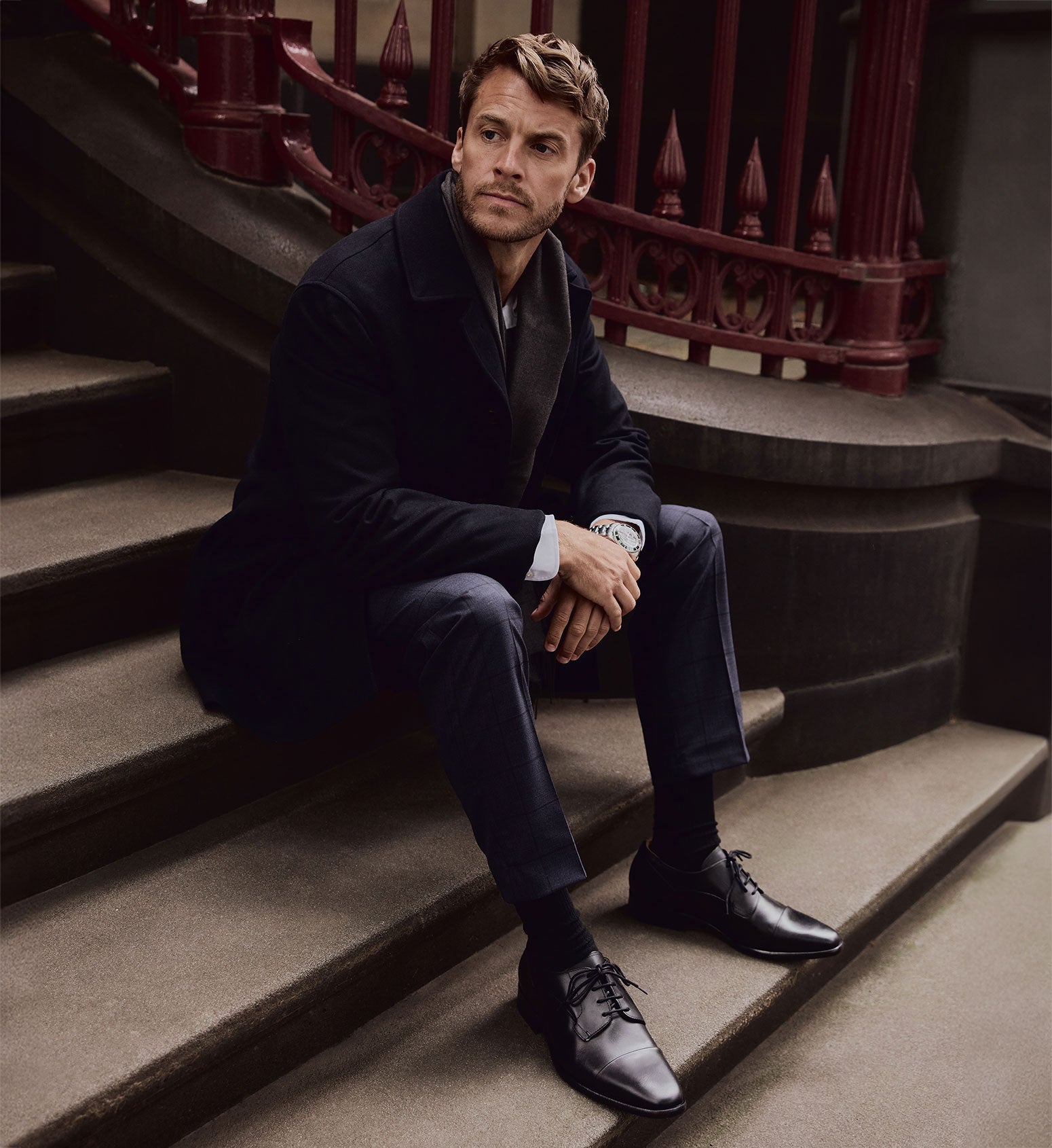 man sitting on stairs outside wearing black dress shoes and a suit