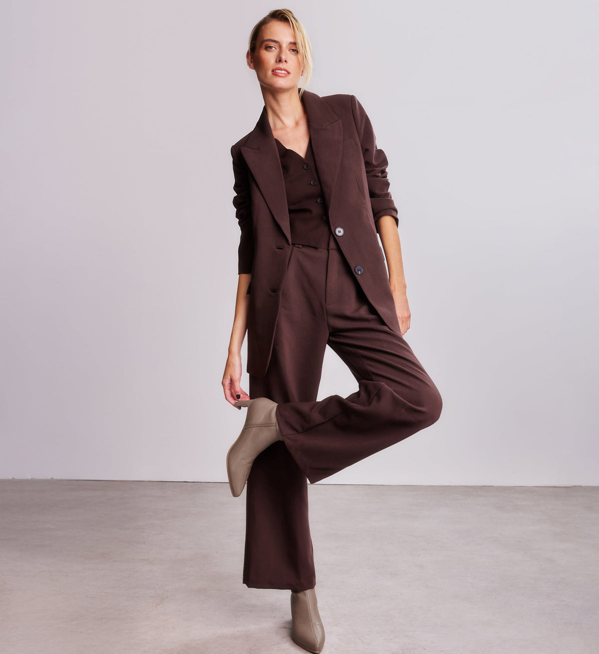 Woman wearing a brown suit with wide-leg pants and a blazer on a plain background with neutral heeled boots