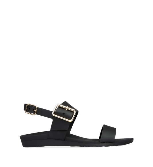 A black flat sandal with buckle straps and a contoured footbed, featuring gold hardware.