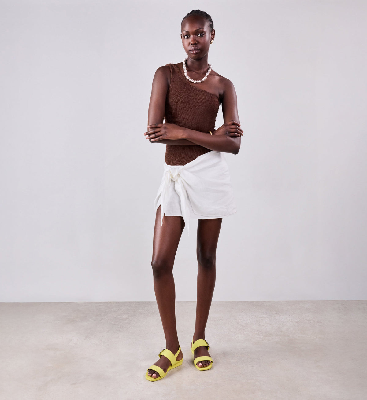 Person wearing a white wrap skirt with yellow sandals on a plain background