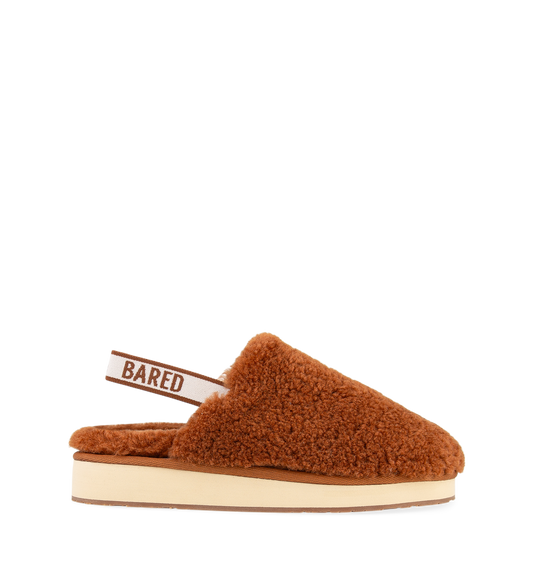 A brown sheepskin slipper with an elastic sling-back strap and the brand name 'BARED' visible on the strap.