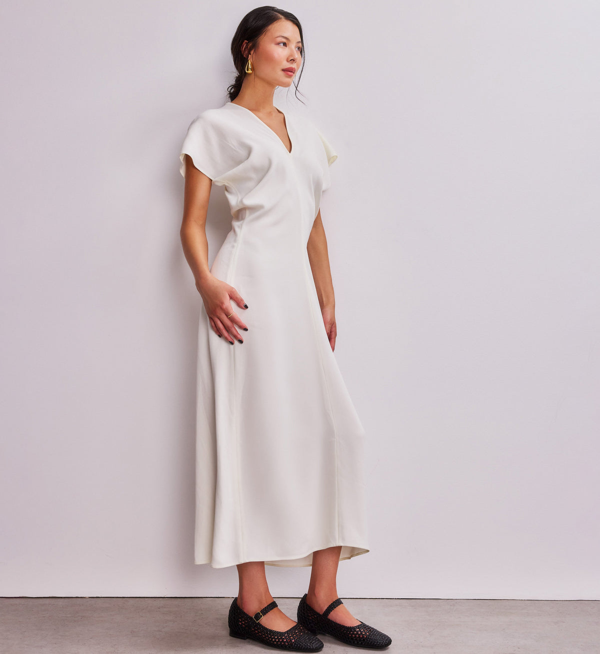 Woman wearing a white dress against a plain background with woven black ballet flats